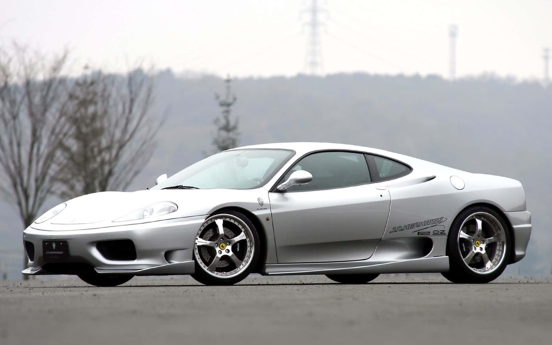 Ferrari 360 Modena 桌布 壁紙 — 一架時尚的銀色法拉利 360 Modena 跑車停泊在開闊的瀝青停車場上，背景有霧氣籠罩的禿樹和山丘。
