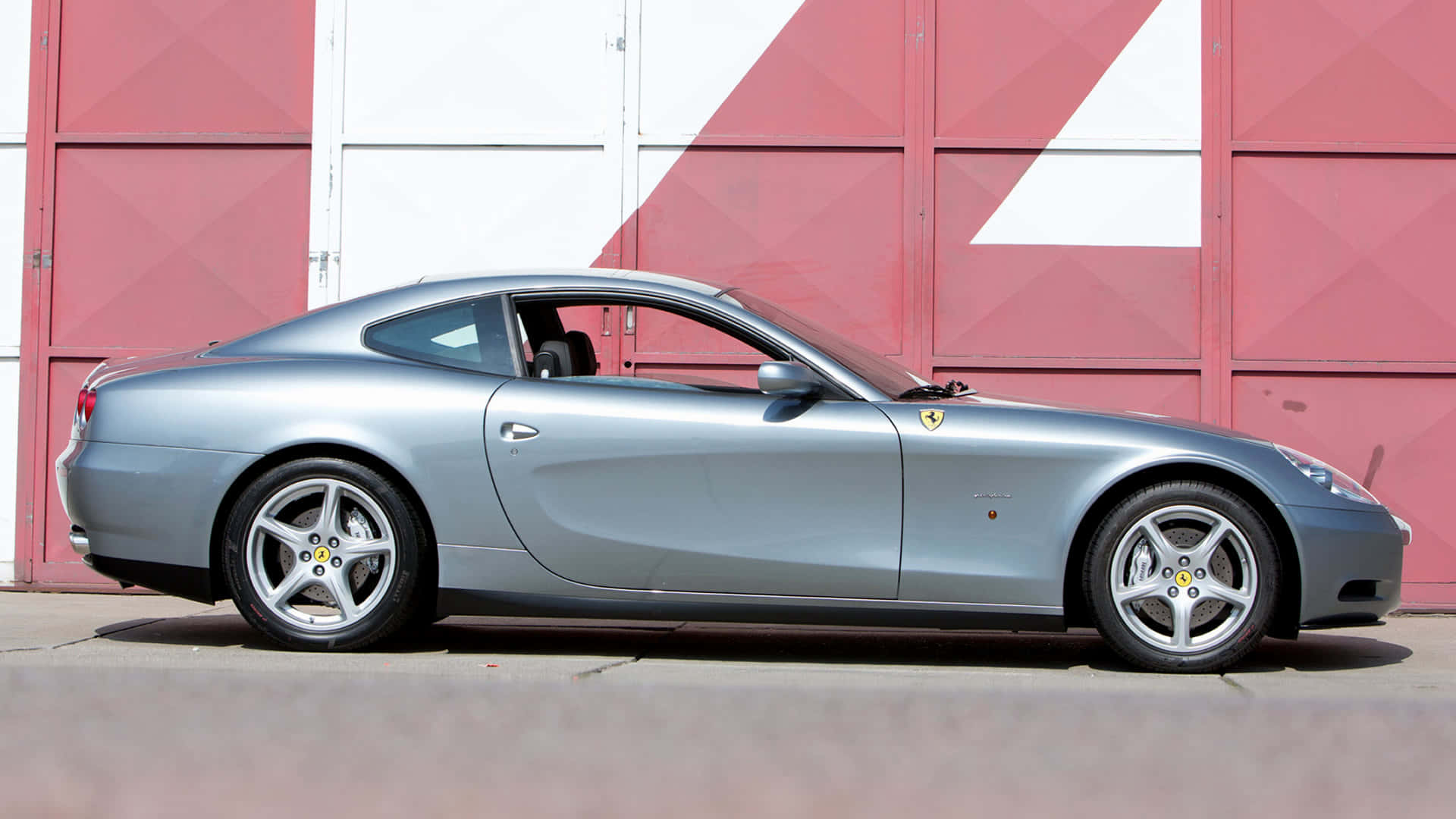 Ferrari 612 Scaglietti 桌布 壁紙 — 一架時尚的銀色法拉利612 Superamerica雙門跑車停放在大膽的紅白幾何車庫門前。