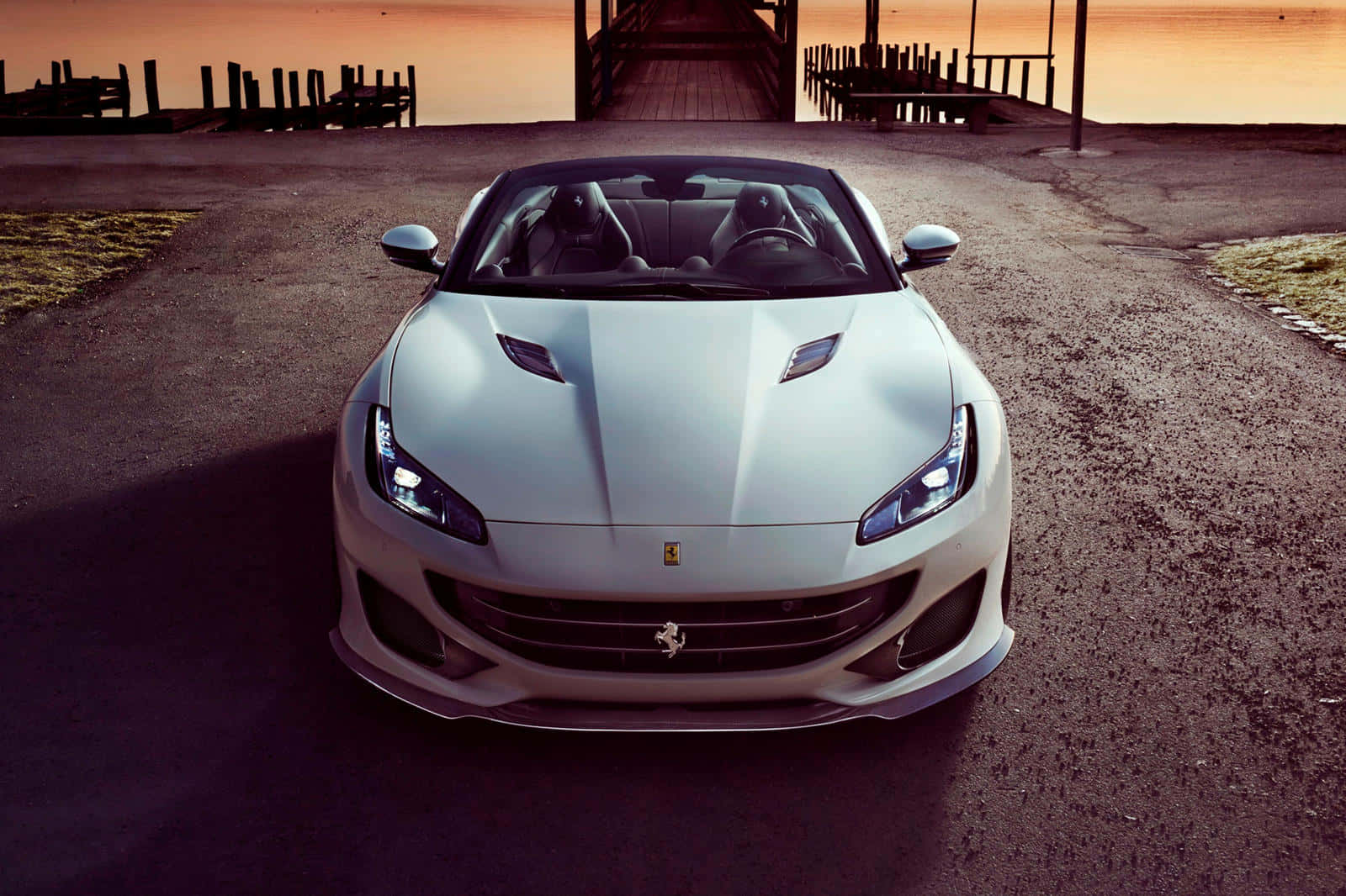 Ferrari Portofino 桌布 壁紙 — 一架時尚的銀色法拉利跑車在日落時分面向前方停在碎石路上，背景是木製碼頭。