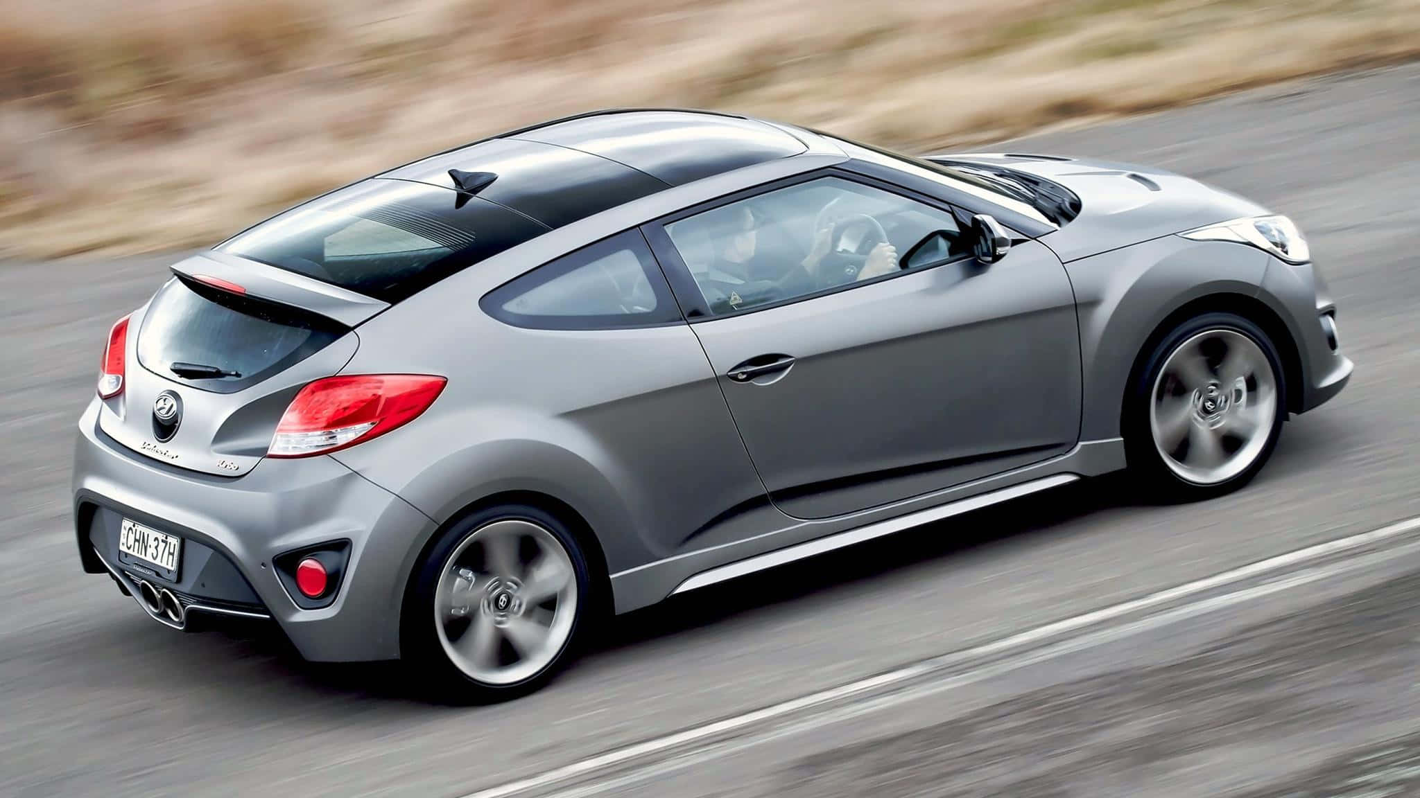 Hyundai Veloster 桌布 壁紙 — 一架時尚的銀色現代Veloster在模糊的道路上疾馳，動態模糊強調了其動感。