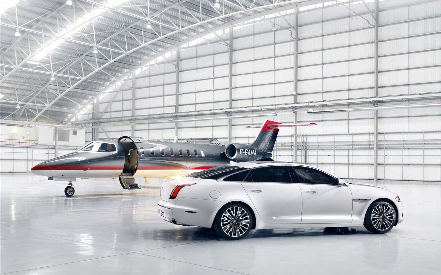 Jet 桌布 壁紙 — 一架時尚的銀色豪華轎車和私人飛機並排停放在一個寬敞明亮、擁有高拱形天花板的機庫內。