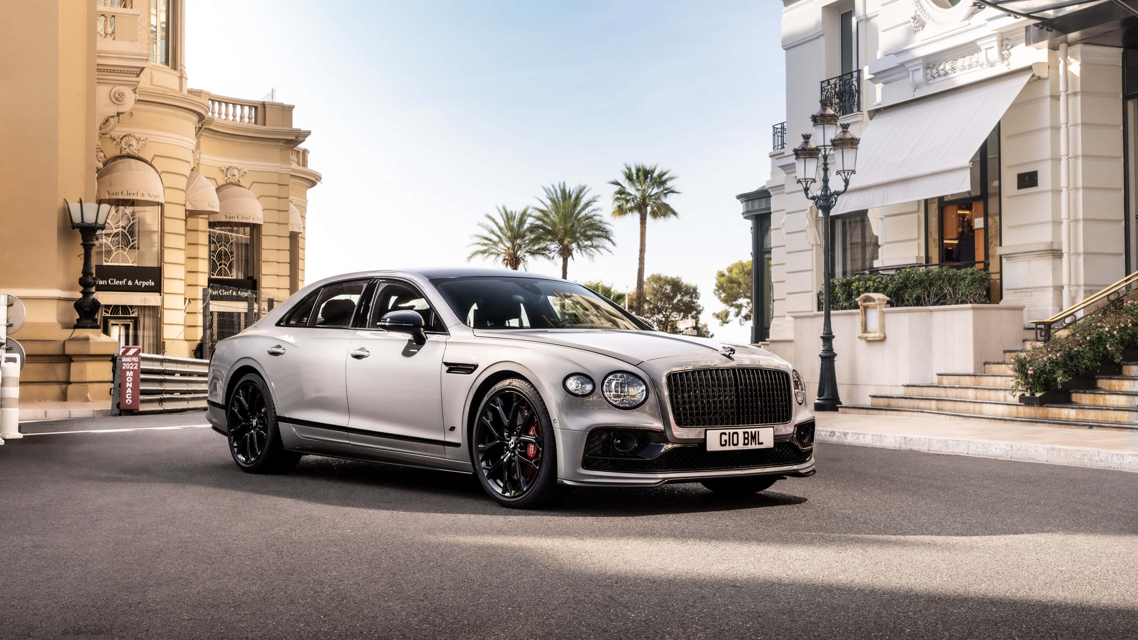 Bentley Mulsanne 桌布 壁紙 — 一架時尚的銀色賓利飛馳配黑色輪圈，停泊在陽光明媚的街道上，兩旁是優雅的建築物和棕櫚樹。