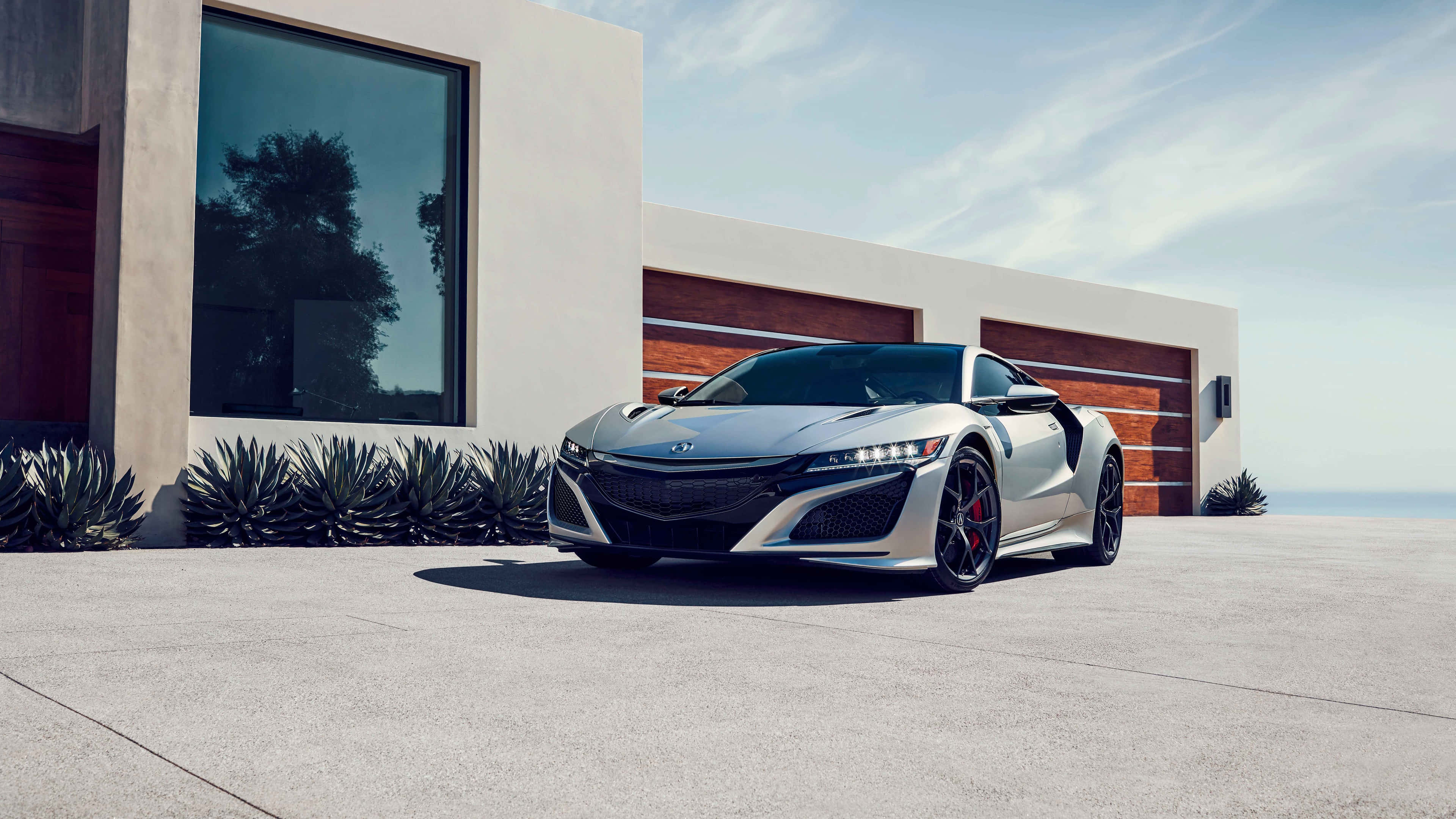 Acura Nsx 桌布 壁紙 — 一架時尚的銀色跑車停泊在混凝土車道上，前面是一棟現代簡約風格的房子，配有大型窗戶和木製車庫門。