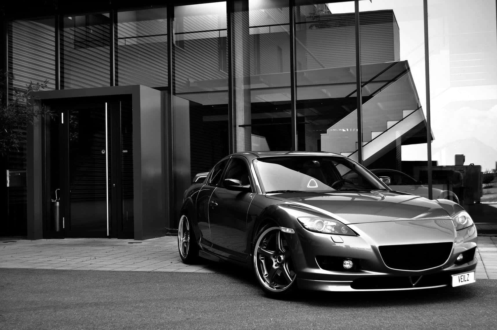 Mazda Rx-8 桌布 壁紙 — 一架時尚的銀色跑車停泊在現代玻璃建築前，以單色呈現。