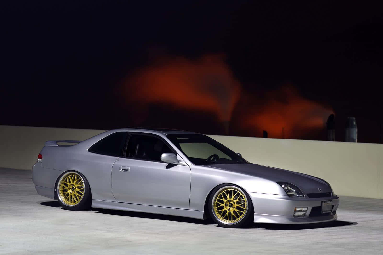 Honda Prelude 桌布 壁紙 — 一架時尚的銀色跑車配金色輪圈在夜間停泊，背景有火熱的橙色煙霧。