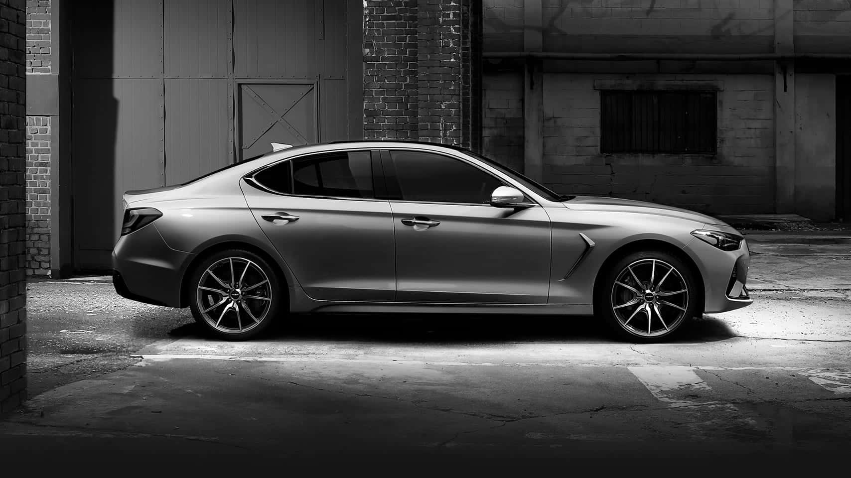 Genesis G70 桌布 壁紙 — 一架時尚的銀色轎車停泊在粗糙的城市小巷中，周圍是磚牆和工業質感，在戲劇性的單色燈光下。