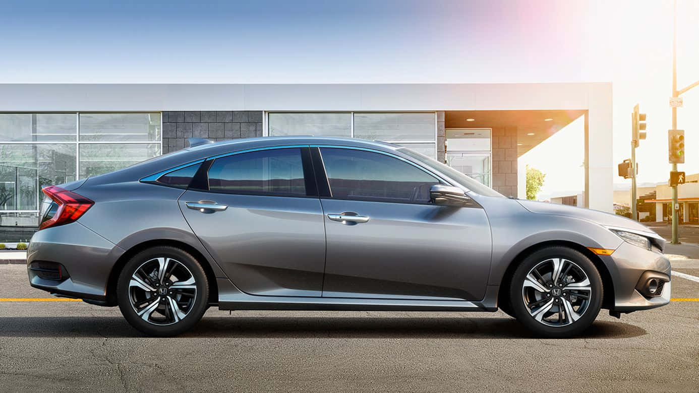 Hatchback 桌布 壁紙 — 一架時尚的銀色轎車停泊在陽光明媚的街道上，旁邊是一座帶玻璃窗的現代建築。