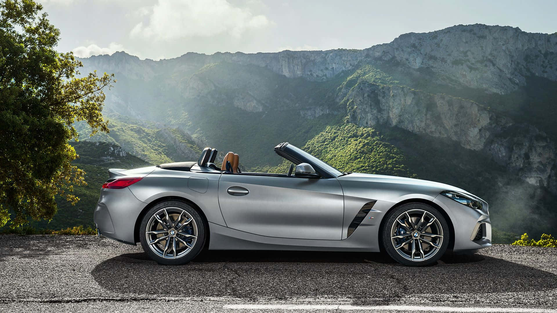 Bmw Z4 桌布 壁紙 — 一架時尚的銀色開篷跑車停泊在山路上，背景是茂密的綠色山丘和岩石山峰。