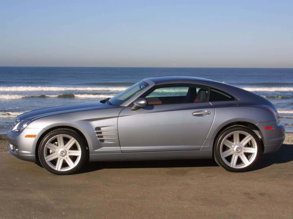 Chrysler Crossfire 桌布 壁紙 — 一架時尚的銀色開篷跑車停泊在沙灘上，背後有海浪拍打，天空晴朗蔚藍。