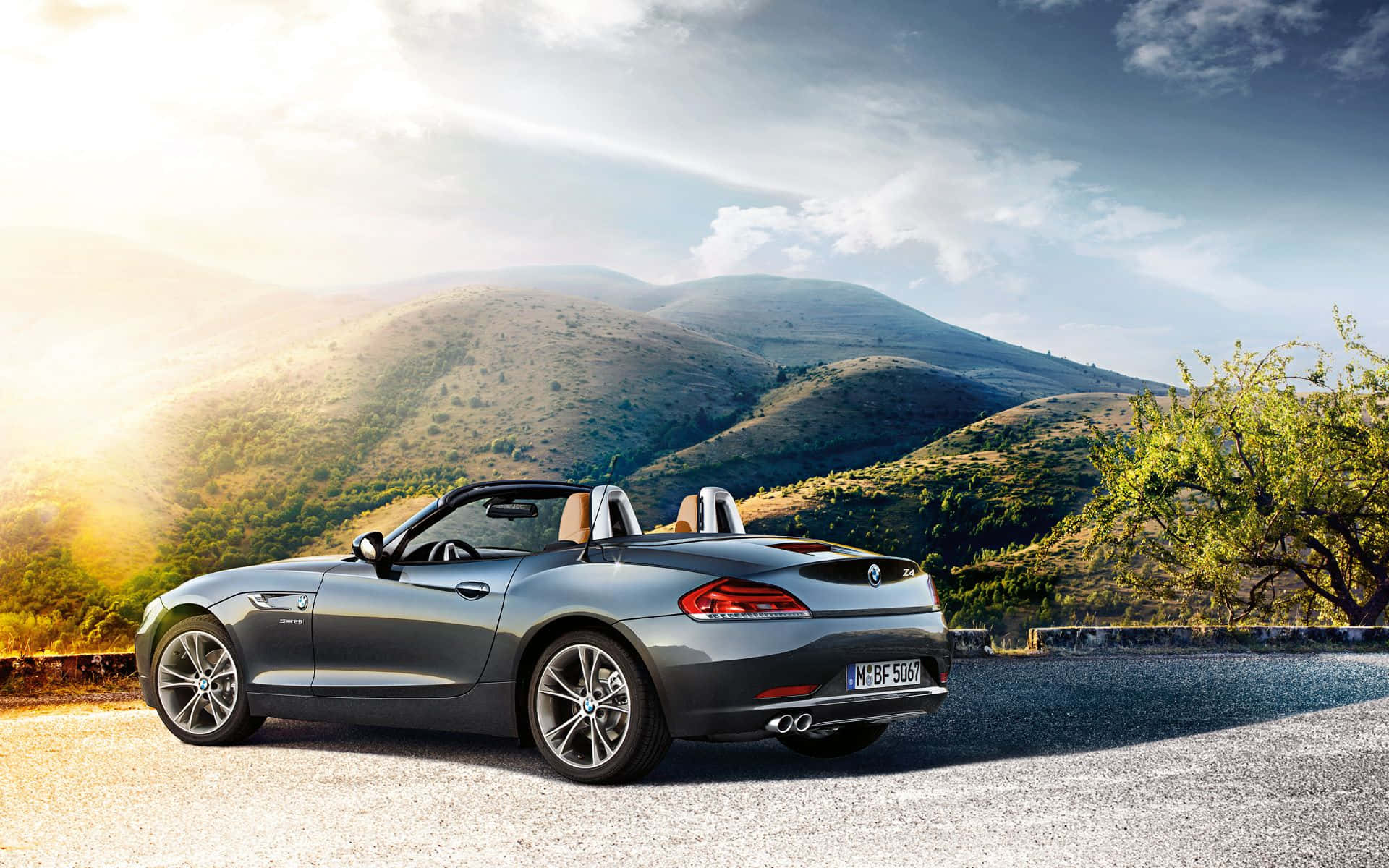 Bmw Z4 桌布 壁紙 — 一架時尚的銀色開篷跑車停泊在碎石路上，背景是陽光普照的起伏山丘和零星樹木。