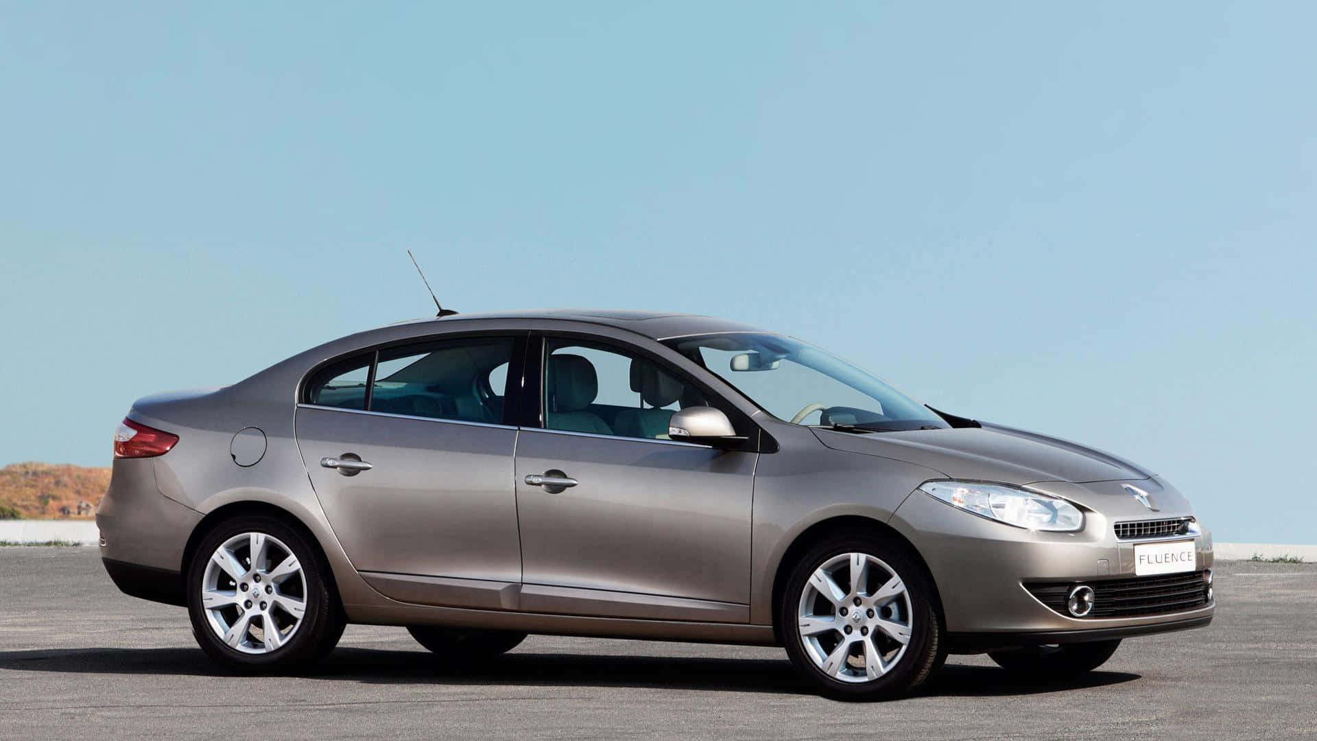 Renault Fluence 桌布 壁紙 — 一架時尚的銀色雷諾 Fluence 房車停泊在開闊的鋪砌停車場上，天空清澈湛藍。