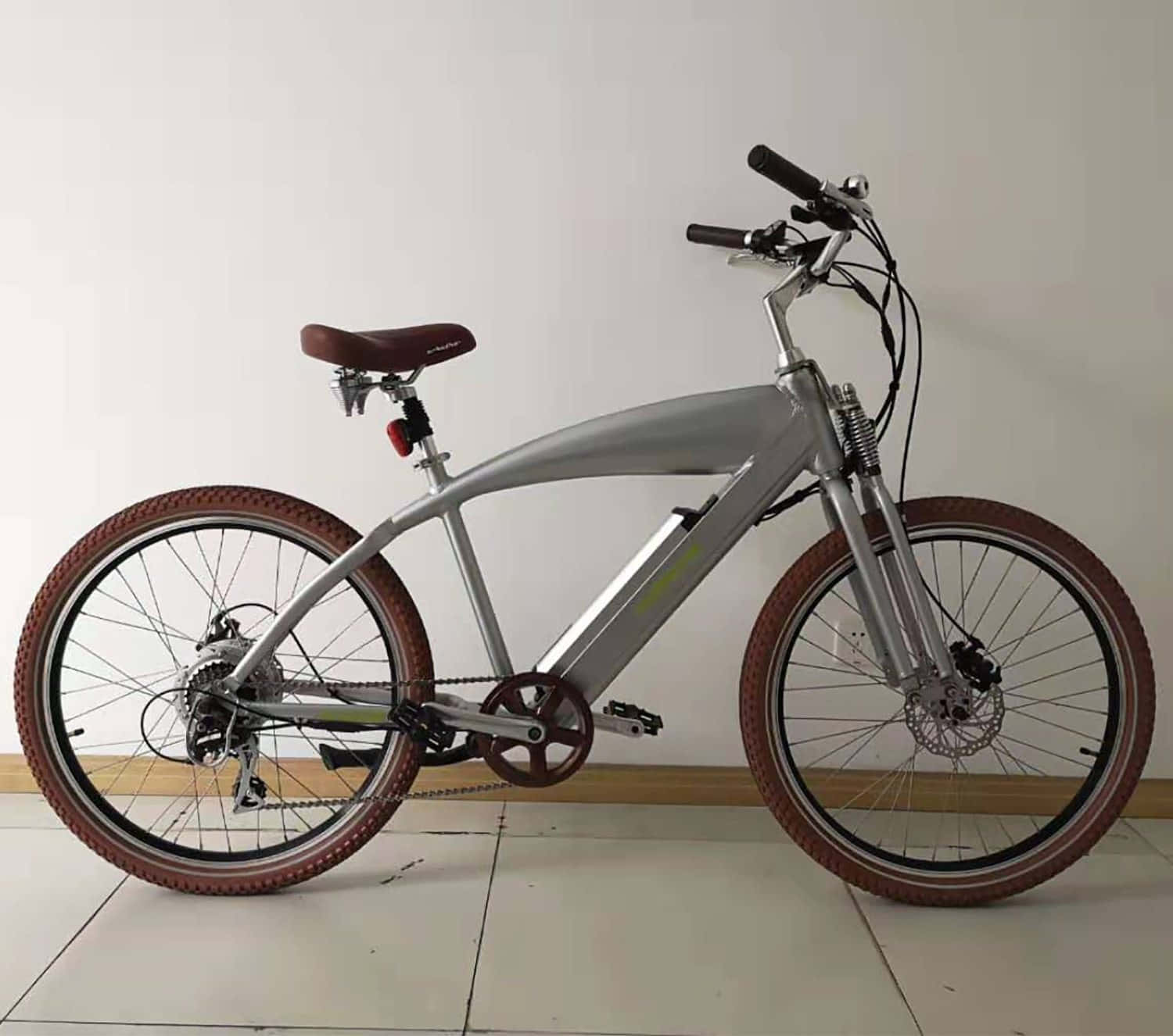 Beach Cruiser 桌布 壁紙 — 一架時尚的銀色電動單車，配備棕色輪胎和座椅，室內靠著純白牆壁停放。