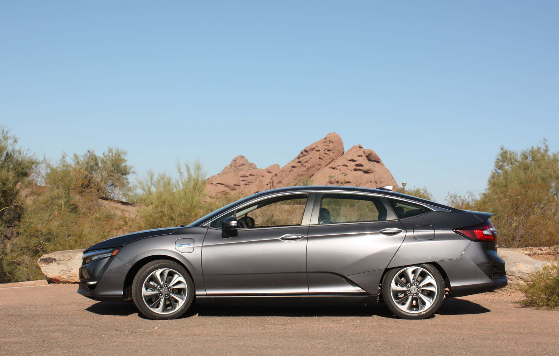 Honda Clarity 桌布 壁紙 — 一架時尚的銀色電動車停在沙漠公路上，周圍有紅色岩層和綠色灌木，天空湛藍清澈。