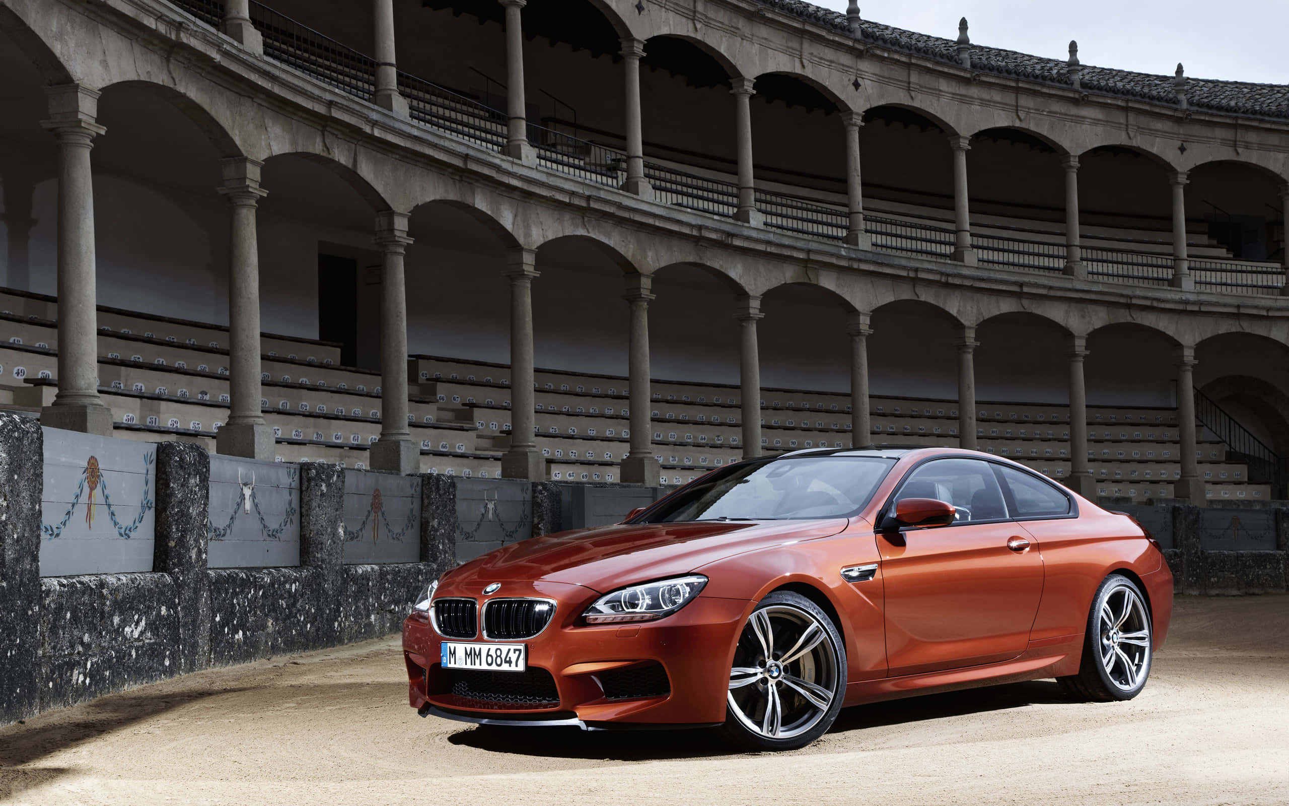 Bmw M6 桌布 壁紙 — 一架時尚的銅色BMW M6雙門跑車停泊在一個空無一人的歷史鬥牛場內，場內有石拱門和分層座位。