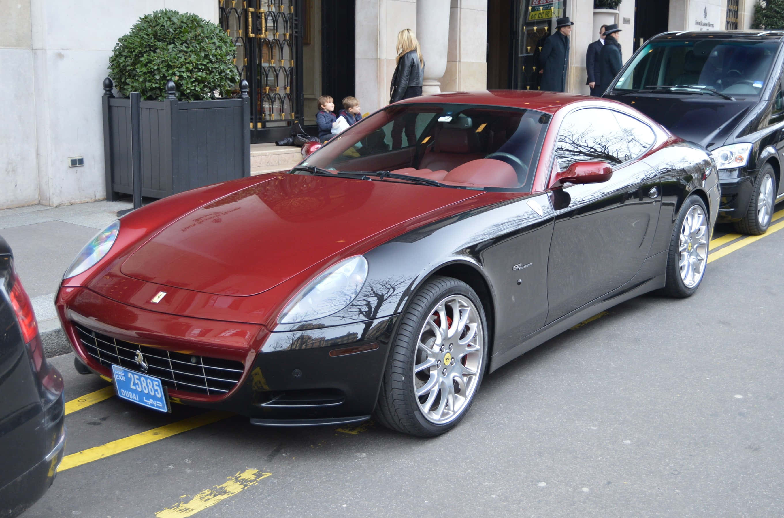 Ferrari 612 Scaglietti 桌布 壁紙 — 一架時尚的雙色法拉利跑車停泊在城市的街道上，背景有行人和建築物。