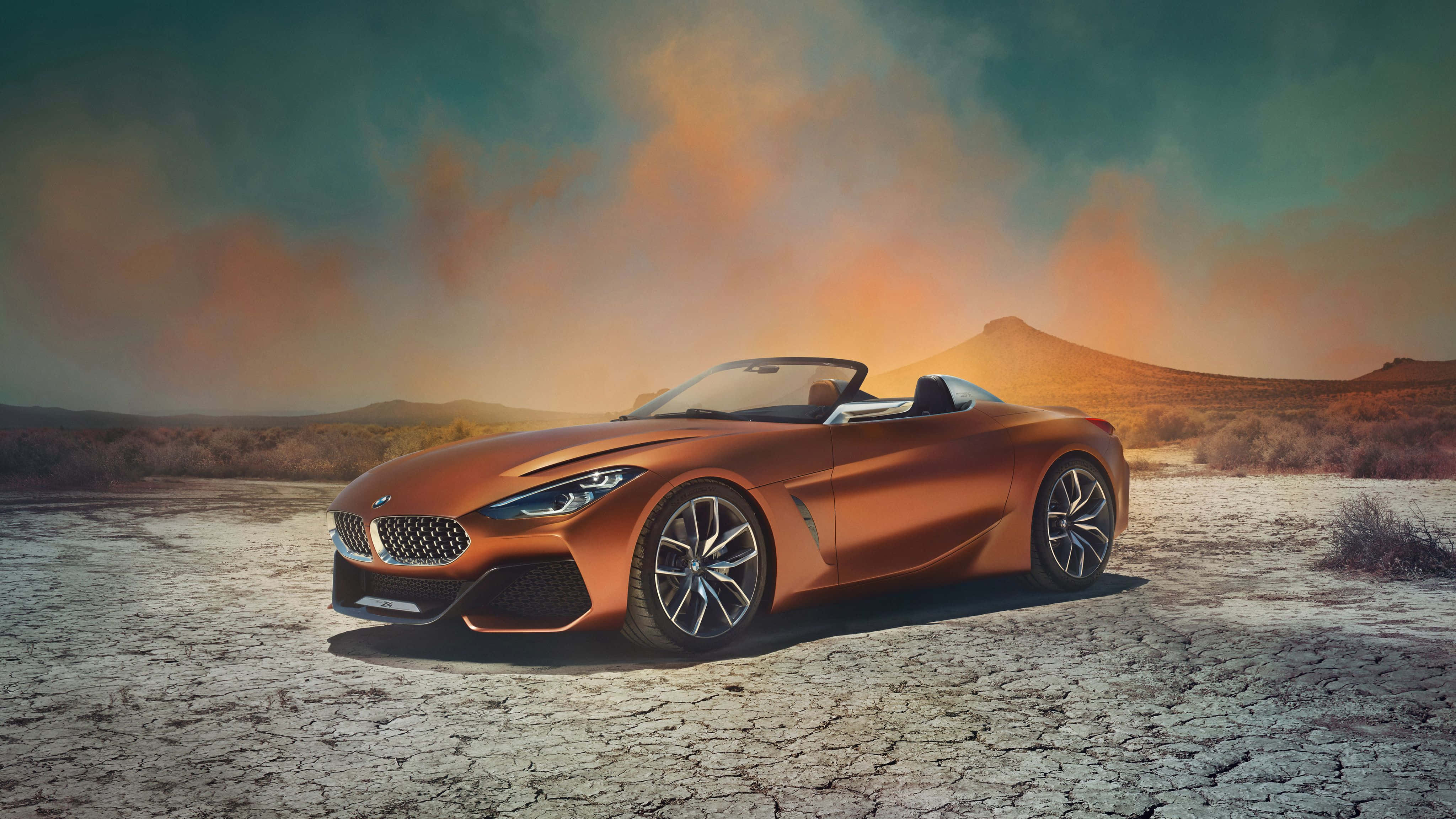 Bmw Z4 桌布 壁紙 — 一架時尚的青銅色開篷跑車停泊在龜裂的沙漠地上，背景是戲劇性的日落天空。