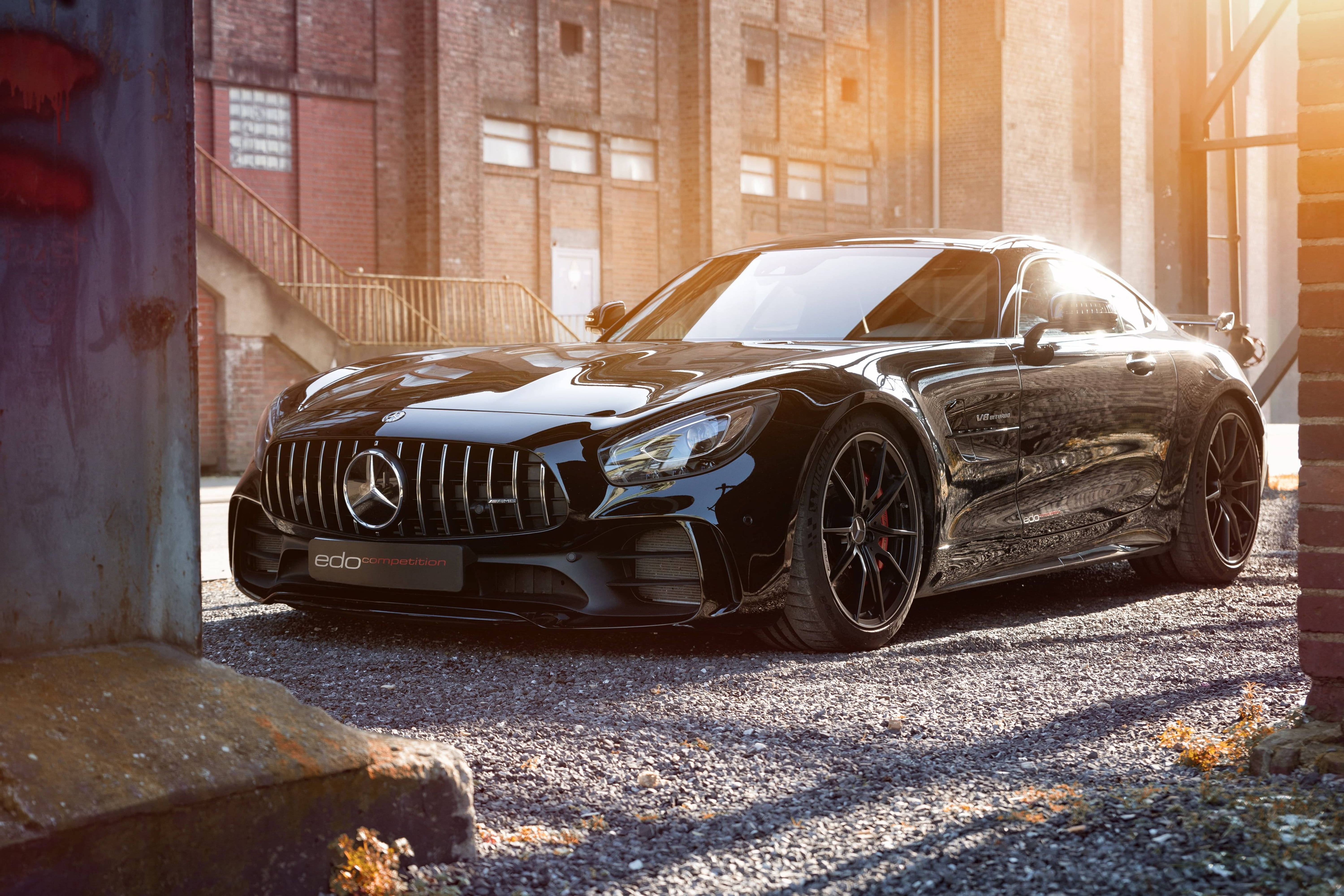 Mercedes 桌布 壁紙 — 一架時尚的黑色 Mercedes-AMG GT 停泊在工業小巷中，陽光在其光澤表面閃爍。