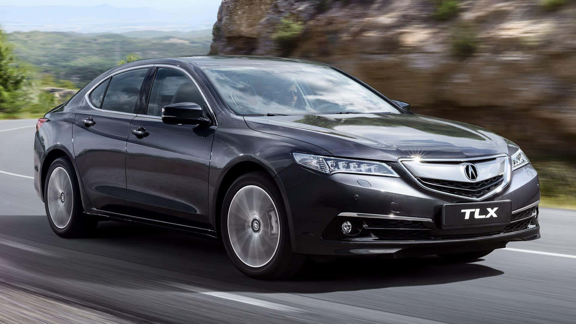 Acura Tlx 桌布 壁紙 — 一架時尚的黑色Acura TLX轎車沿著蜿蜒的山路疾馳，背景是模糊的綠色山丘和岩石峭壁。