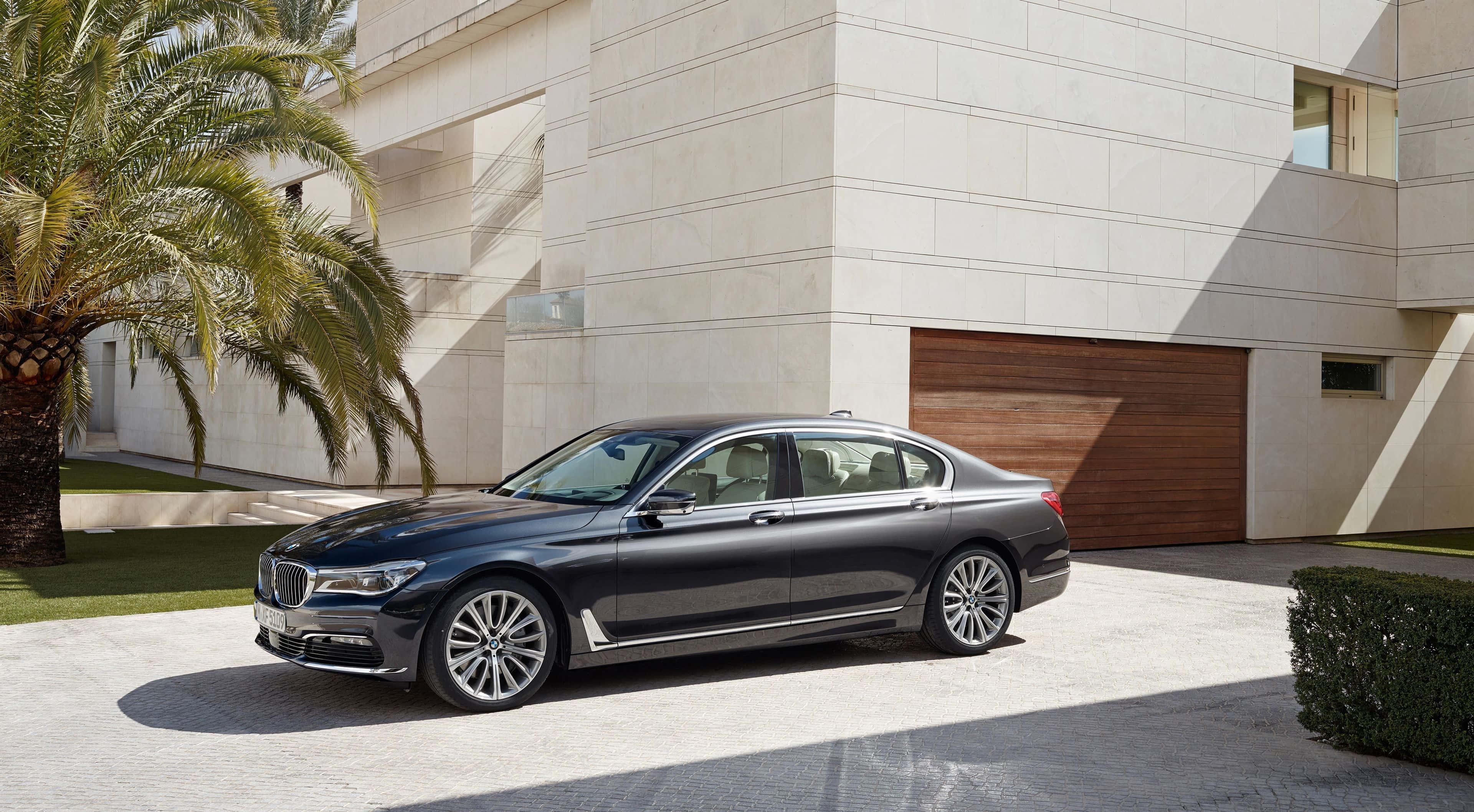 Bmw 7 Series 桌布 壁紙 — 一架時尚的黑色BMW 7系轎車停泊在陽光普照的車道上，旁邊是一座現代住宅和一棵棕櫚樹。