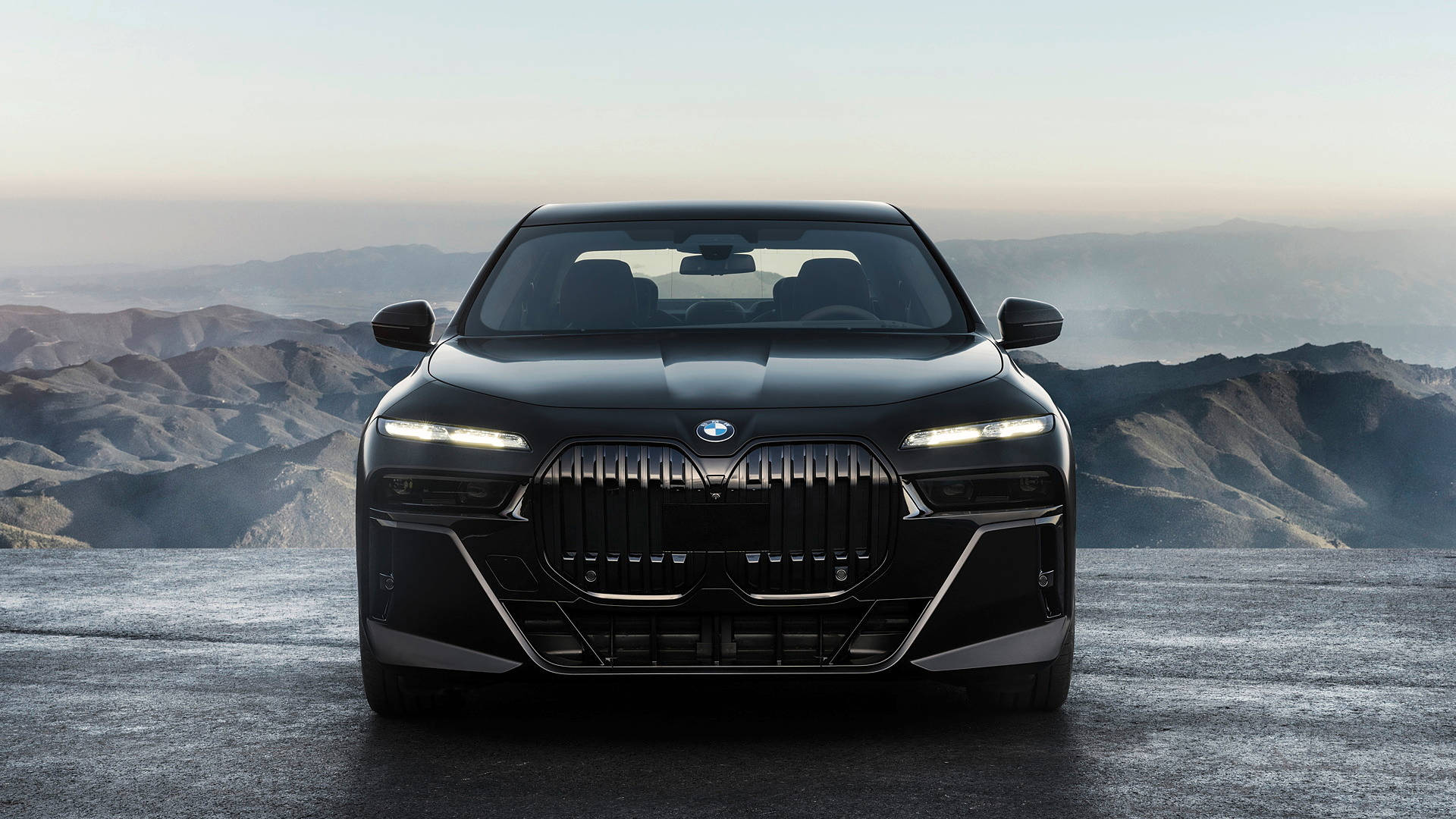 戶外 桌布 壁紙 — 一架時尚的黑色BMW i7電動轎車在懸崖邊緣向前，俯瞰黎明時分霧氣繚繞的山脈。