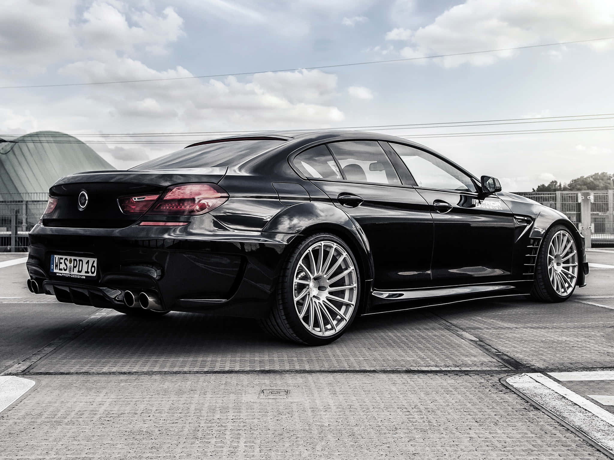 Bmw M6 桌布 壁紙 — 一架時尚的黑色BMW M6雙門轎跑車，配備定制銀色輪圈，停泊在紋理路面上，天空多雲。