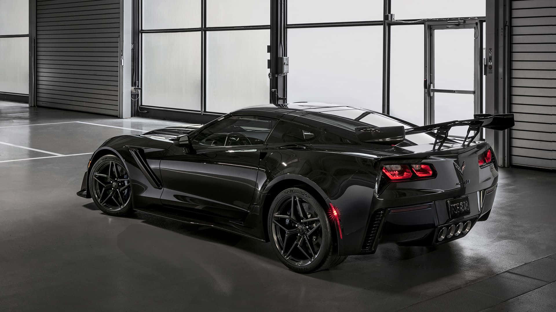 corvette 桌布 壁紙 — 一架時尚的黑色Corvette跑車，帶有發光的紅色尾燈，停放在現代工業車庫內。