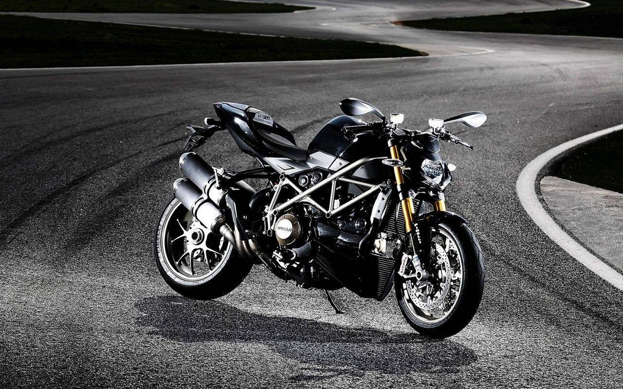 機車 桌布 壁紙 — 一架時尚的黑色Ducati電單車配金色前叉，夜晚停在空無一人的瀝青路上，在戲劇性的燈光下投射出銳利的陰影。