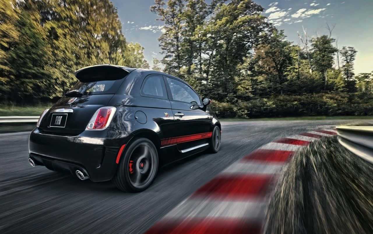 Fiat 500l 桌布 壁紙 — 一架時尚的黑色Fiat 500 Abarth在蜿蜒的森林道路上飛馳，紅白條紋護欄模糊掠過。
