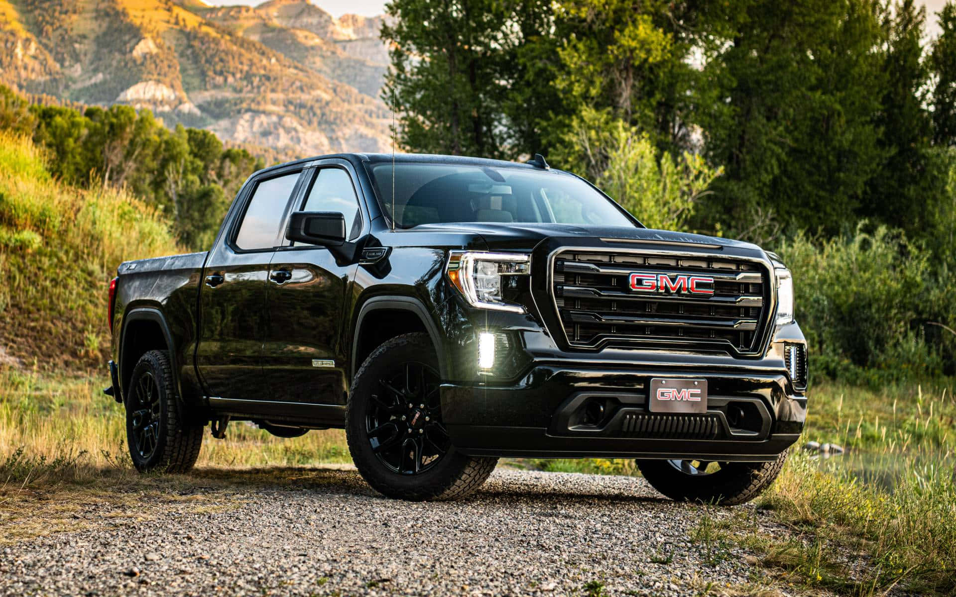 Gmc Sierra 桌布 壁紙 — 一架時尚的黑色GMC Sierra皮卡車停在碎石路上，背景有山脈和樹木。