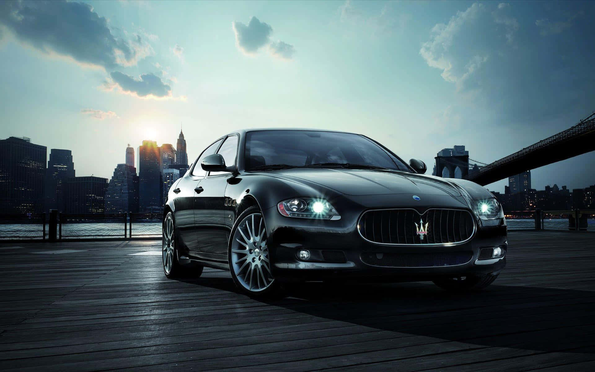 Best Car 桌布 壁紙 — 一架時尚的黑色Maserati房車在日落時分的木製碼頭上閃閃發光，背景是城市天際線和橋樑。