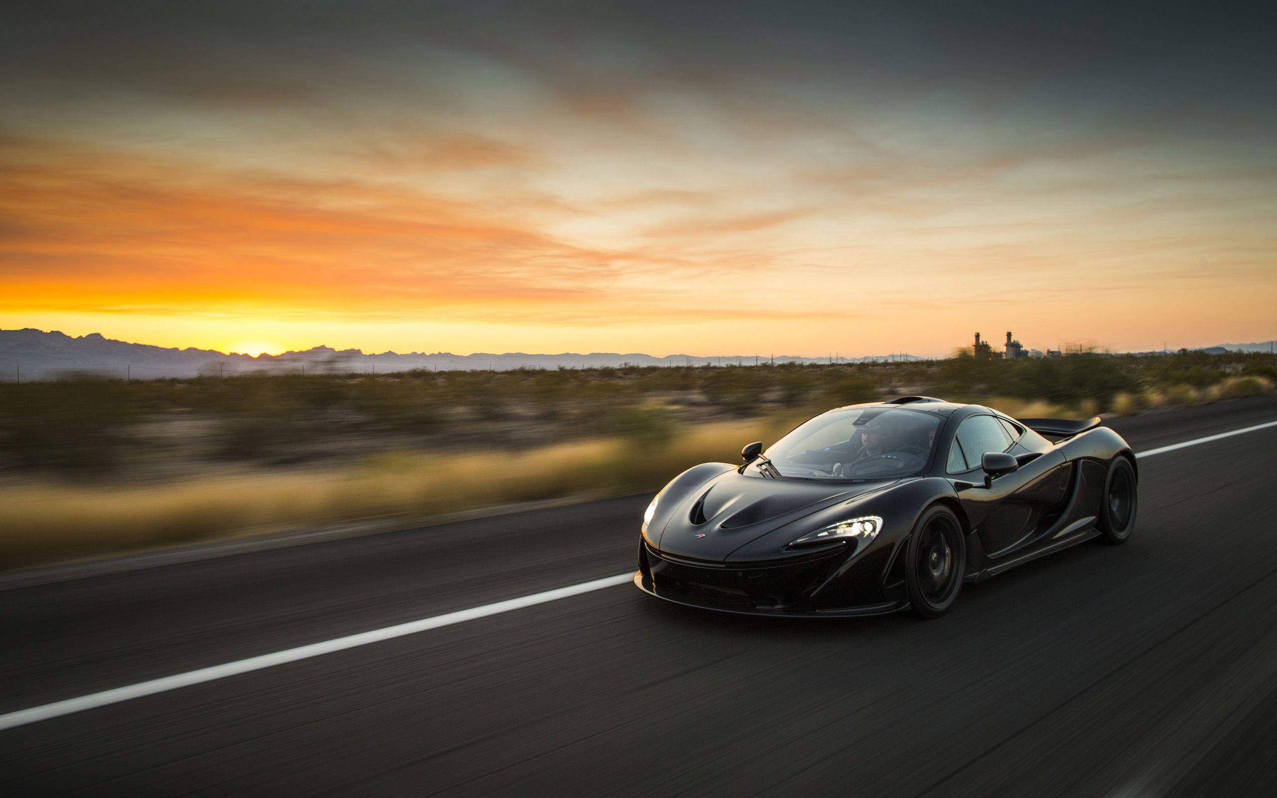 日落 桌布 壁紙 — 一架時尚的黑色McLaren超級跑車在日落時分沿沙漠高速公路疾馳，帶有模糊的動感和溫暖的橙色天空。
