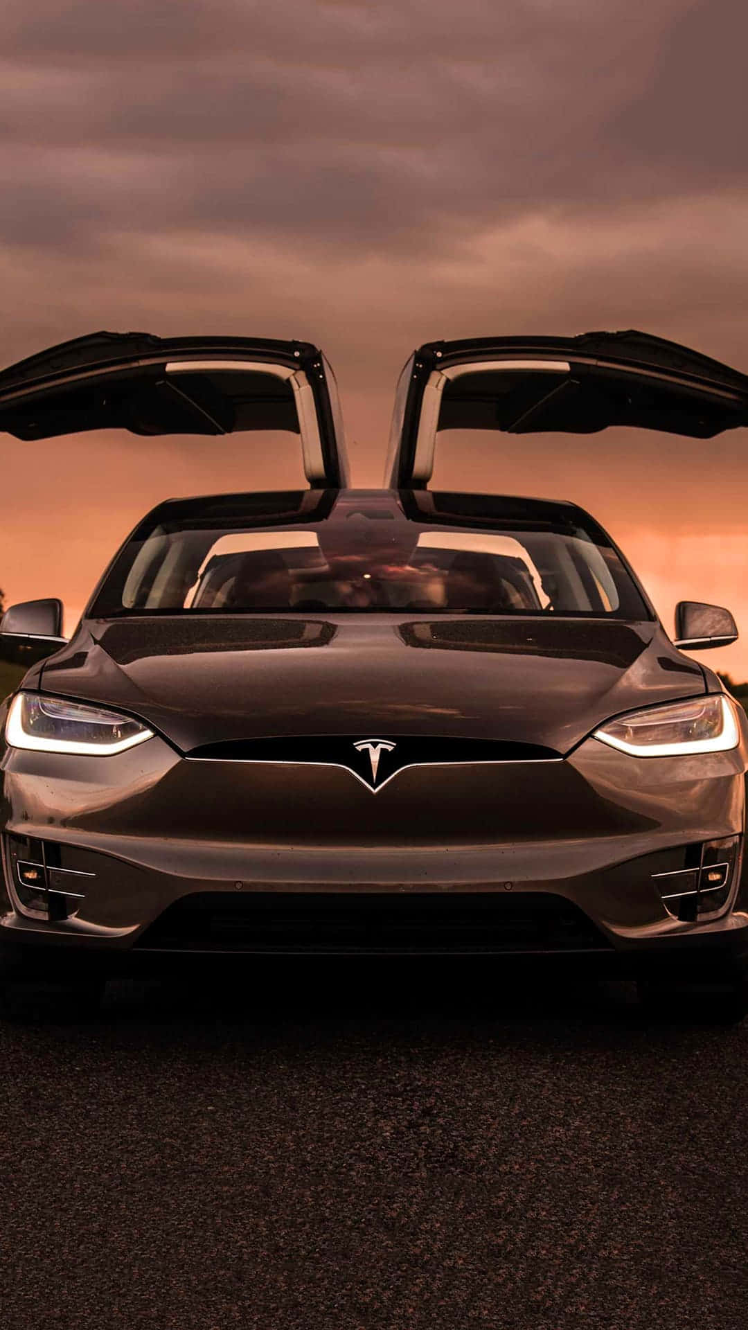 tesla 桌布 壁紙 — 一架時尚的黑色Tesla，打開鷗翼車門，在戲劇性的日落天空下蓄勢待發。