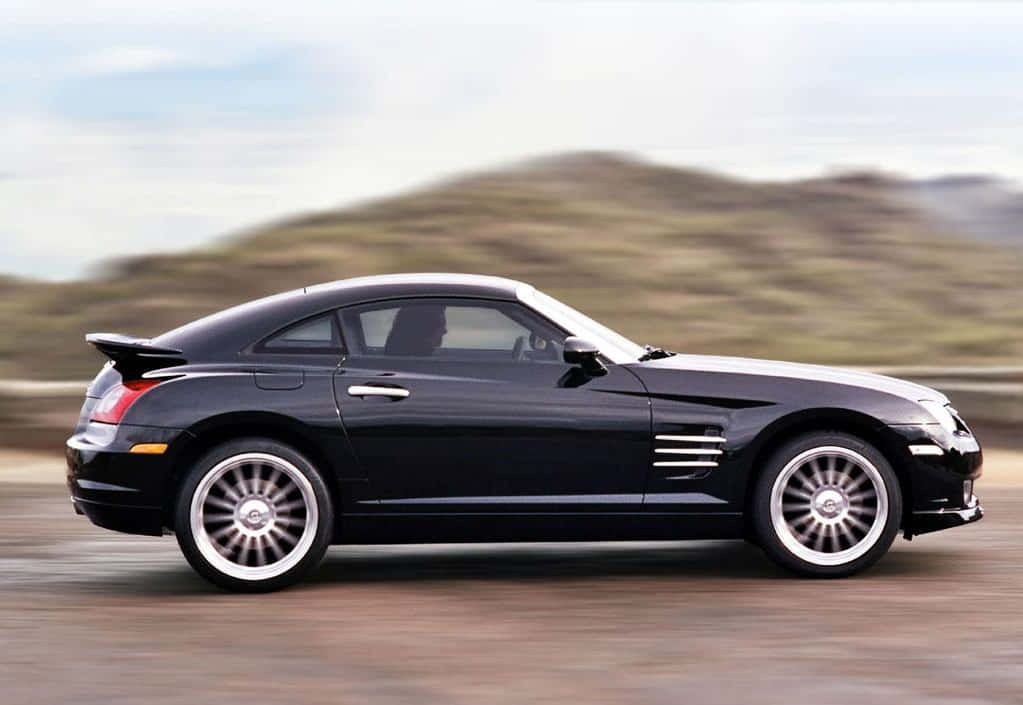 Chrysler Crossfire 桌布 壁紙 — 一架時尚的黑色克萊斯勒 Crossfire 跑車在沙漠公路上飛馳，背景是模糊的山丘。