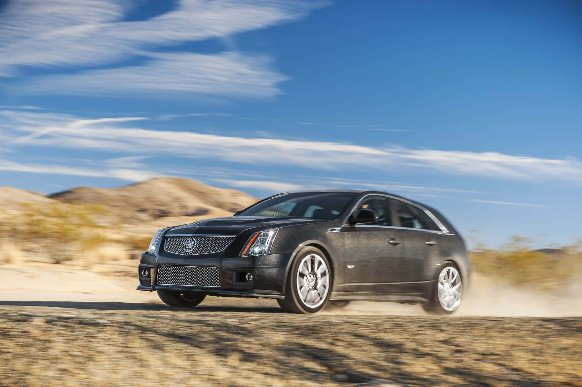 Cadillac Cts 桌布 壁紙 — 一架時尚的黑色凱迪拉克轎車在塵土飛揚的沙漠公路上疾馳，天空湛藍，白雲輕飄。