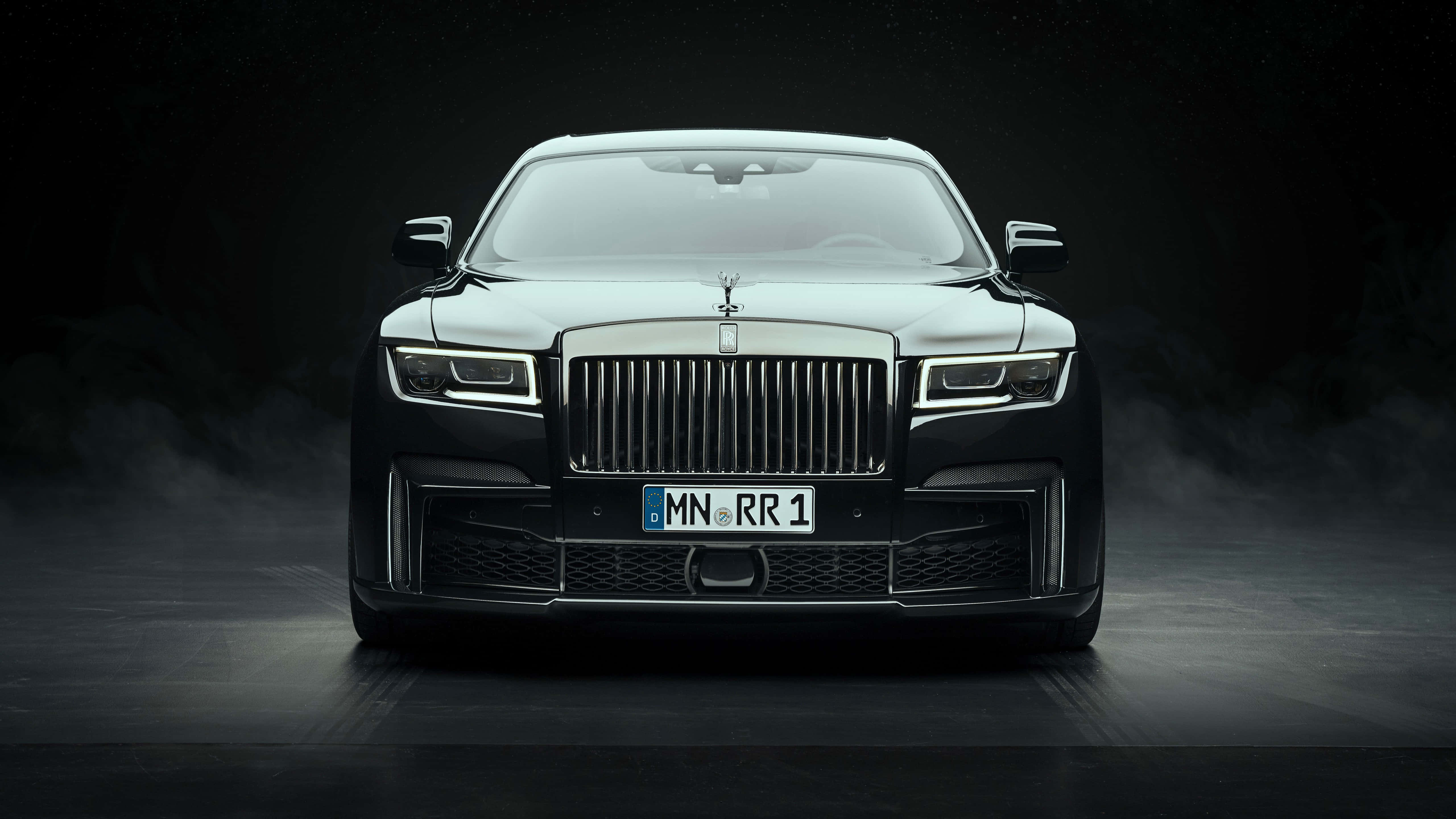Rolls Royce 桌布 壁紙 — 一架時尚的黑色勞斯萊斯Phantom在聚光燈下戲劇性地矗立，霧氣在其標誌性格柵和發光的車頭燈周圍旋轉。