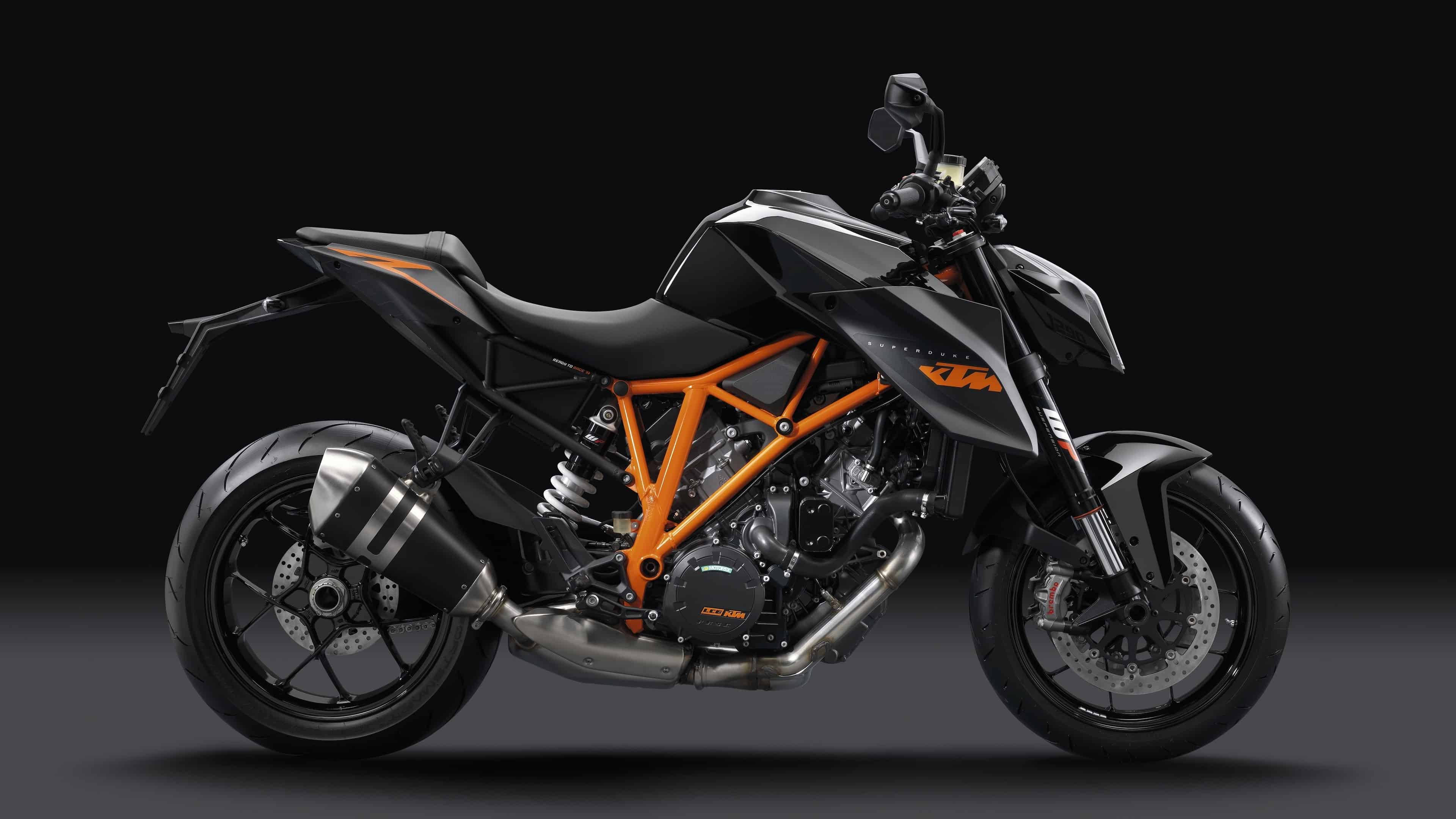 ktm rc 200 桌布 壁紙 — 一架時尚的黑色和橙色KTM電單車，帶有外露引擎和鍍鉻排氣管，在黑暗的攝影棚中配合戲劇性燈光。