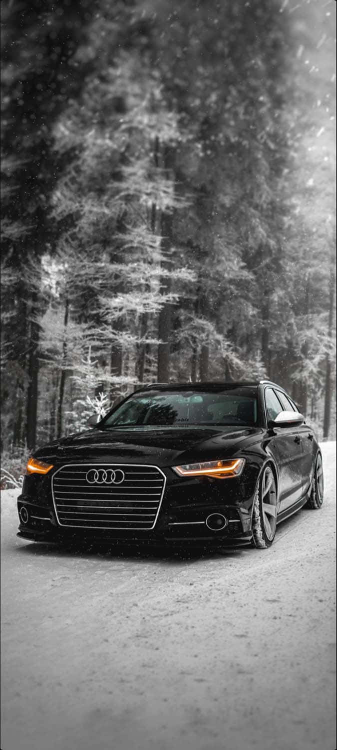  壁紙 — 一架時尚的黑色奧迪轎車，橙色頭燈閃爍，停在積雪的森林道路上，雪花飄落。