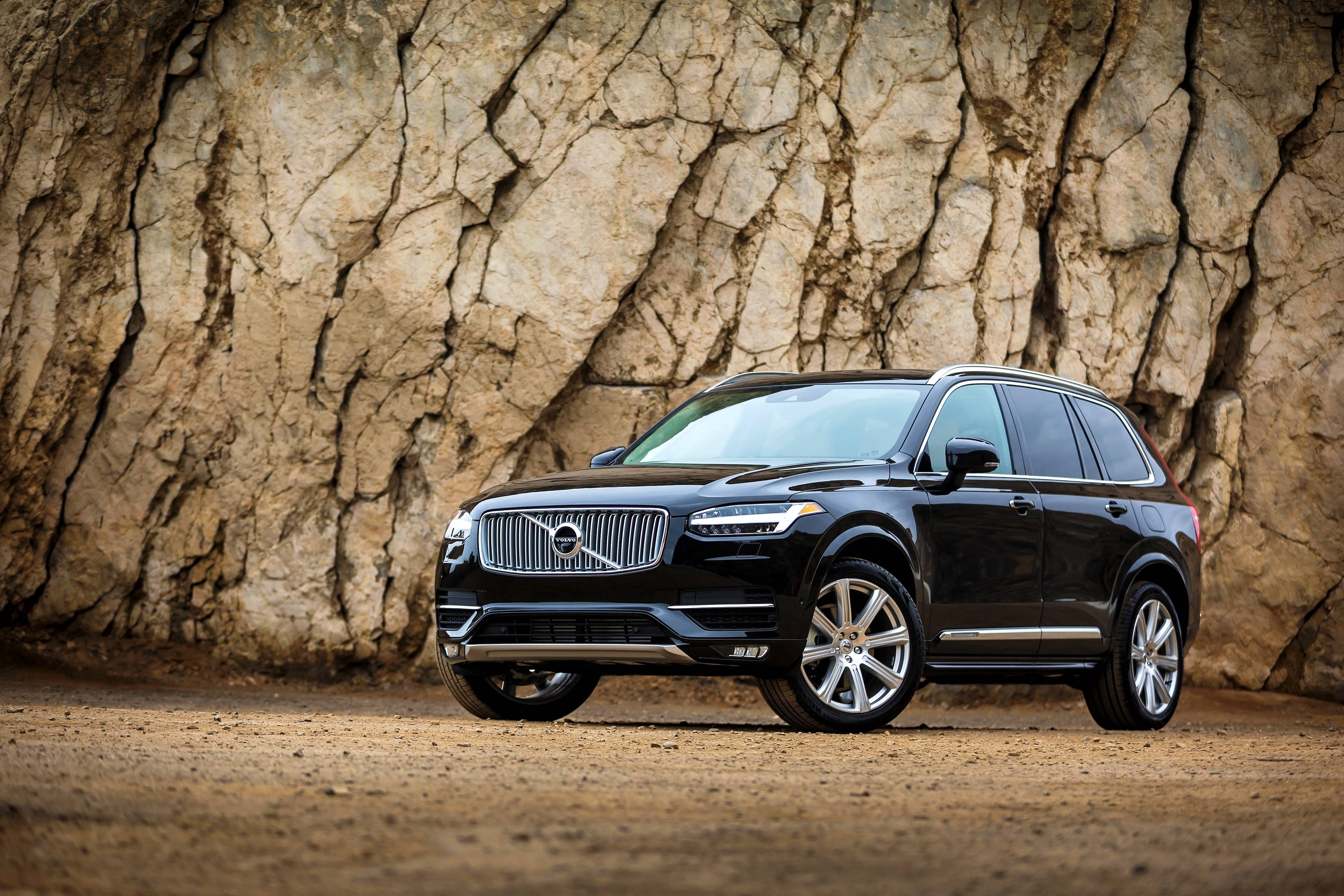 Jet Black Volvo SUV 壁紙 — 一架時尚的黑色富豪XC90 SUV停泊在泥土上，前面是粗糙紋理的岩石峭壁。