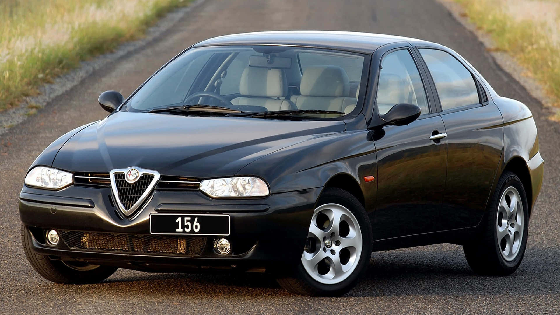 Alfa Romeo 156 桌布 壁紙 — 一架時尚的黑色愛快羅密歐156房車停泊在碎石路上，背景是草地田野。