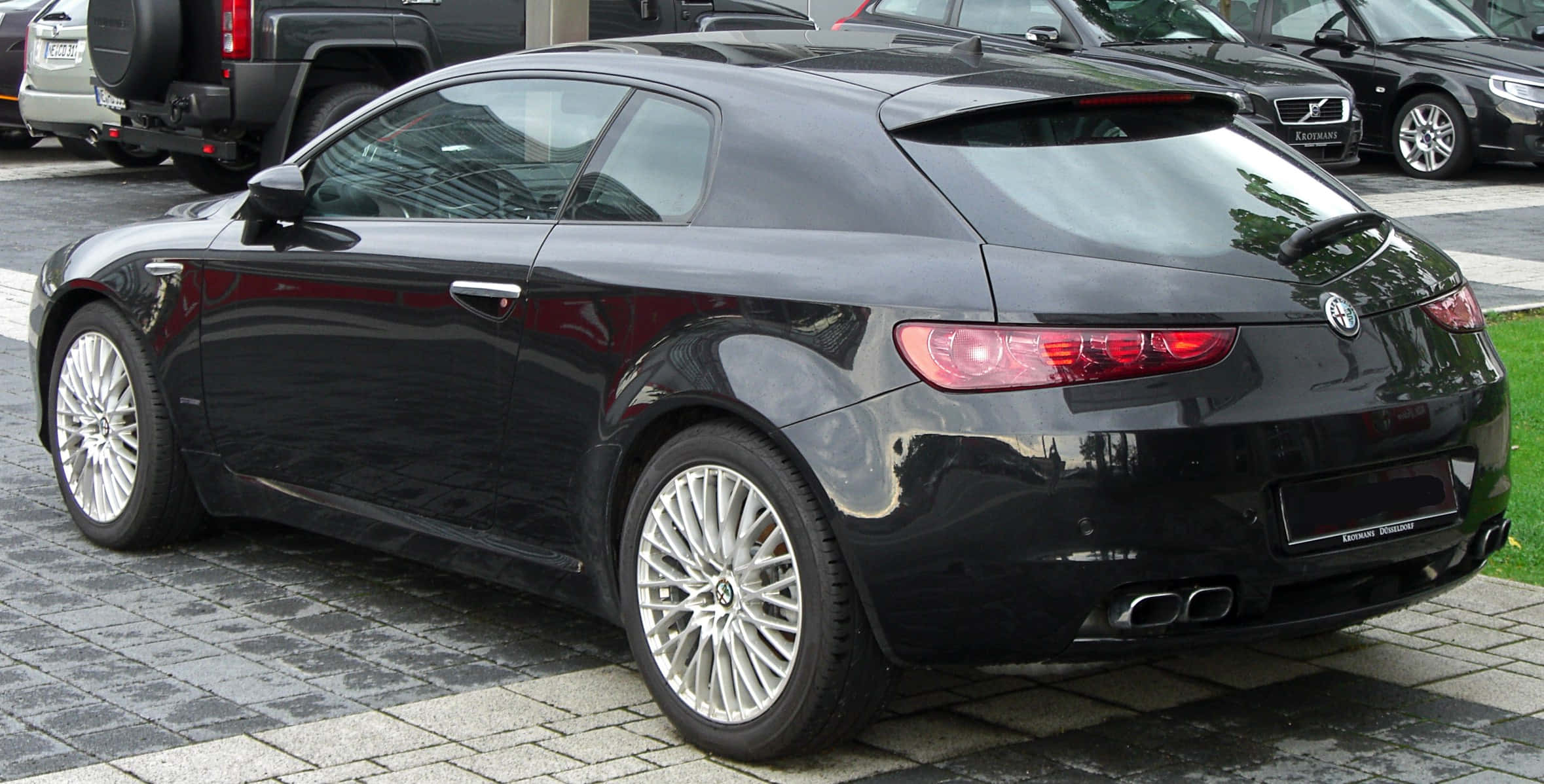 Alfa Romeo Brera 桌布 壁紙 — 一架時尚的黑色愛快羅密歐跑車雙門轎跑車停泊在鋪砌的停車場上，背景可見其他車輛。