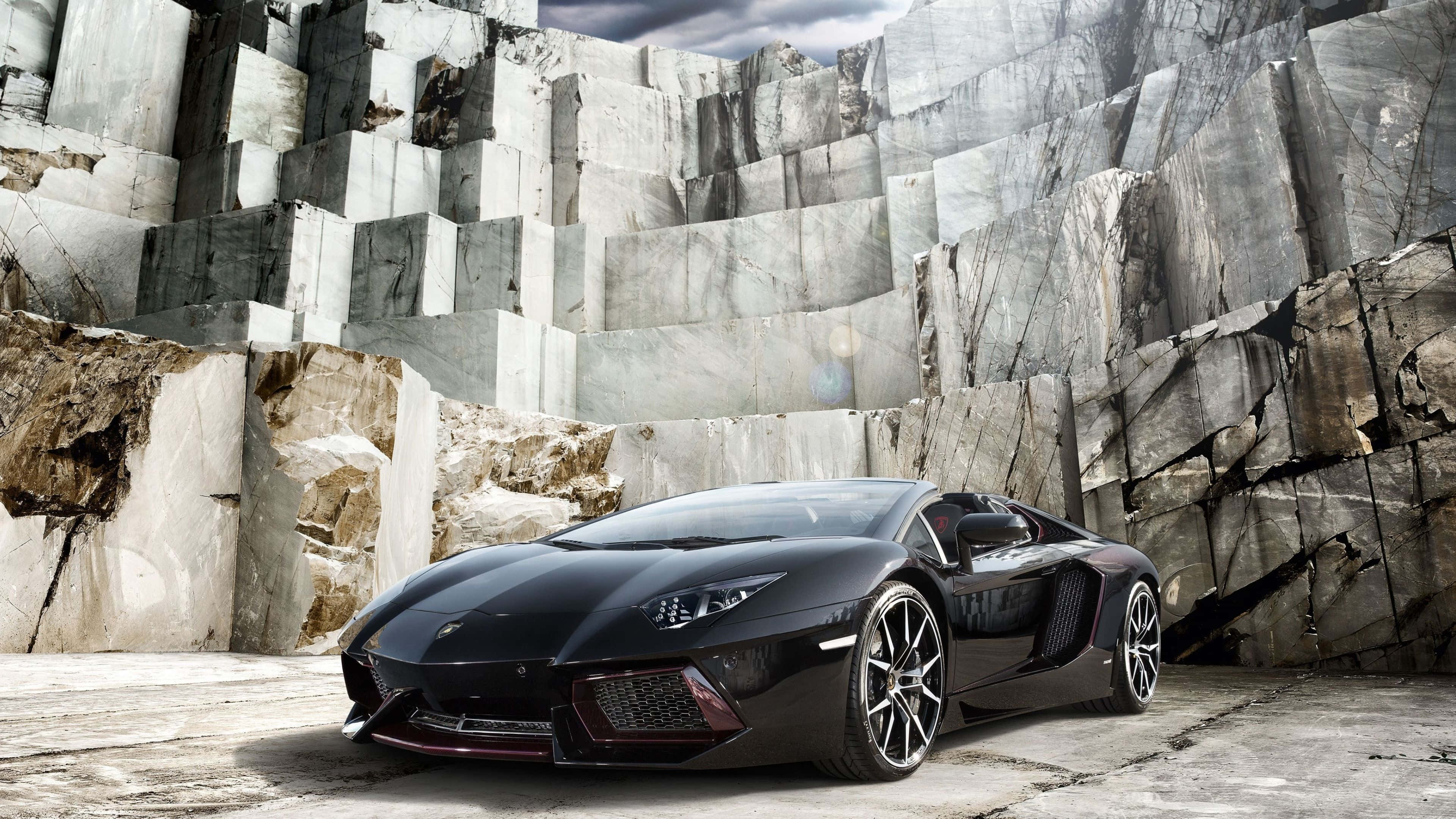 林寶堅尼 4K 桌布 壁紙 — 一架時尚的黑色林寶堅尼 Aventador 停泊在巨大大理石懸崖前，天空多雲。