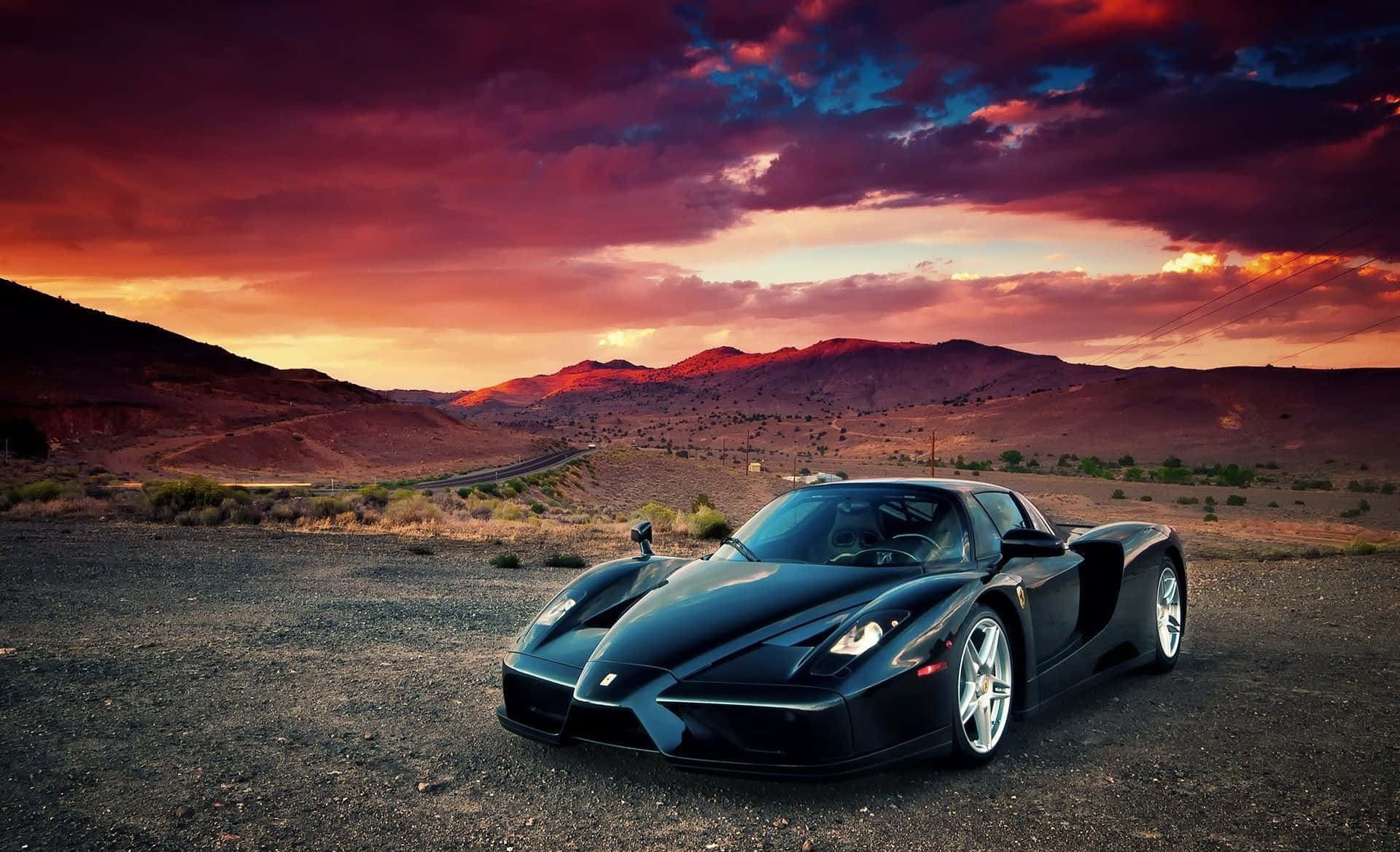 Ferrari Enzo 桌布 壁紙 — 一架時尚的黑色法拉利Enzo停泊在碎石上，背景是戲劇性的日落天空，有火燒雲和遠山。