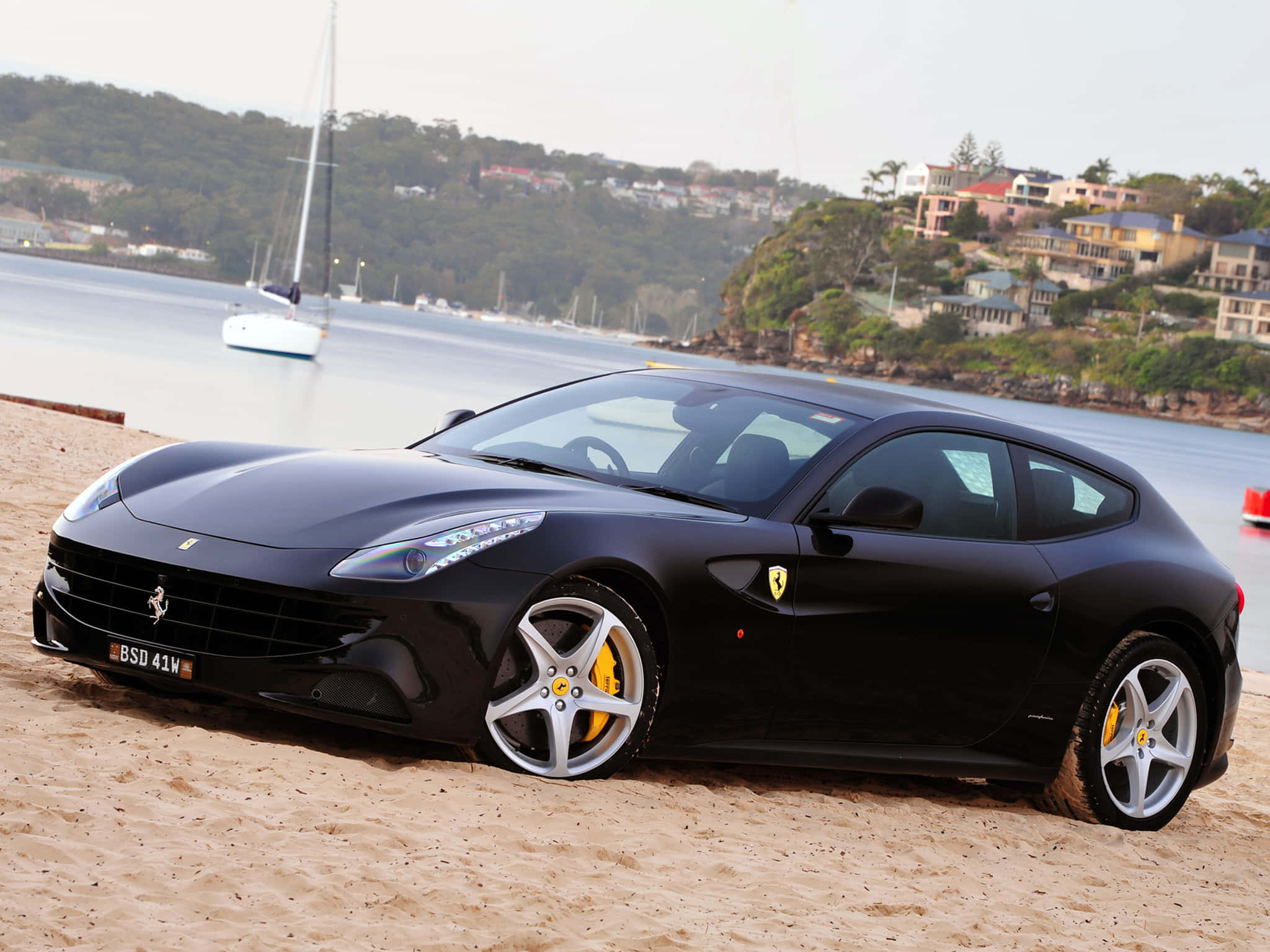 Ferrari Ff 桌布 壁紙 — 一架時尚的黑色法拉利FF停在沙灘上，背景有帆船和沿海房屋。