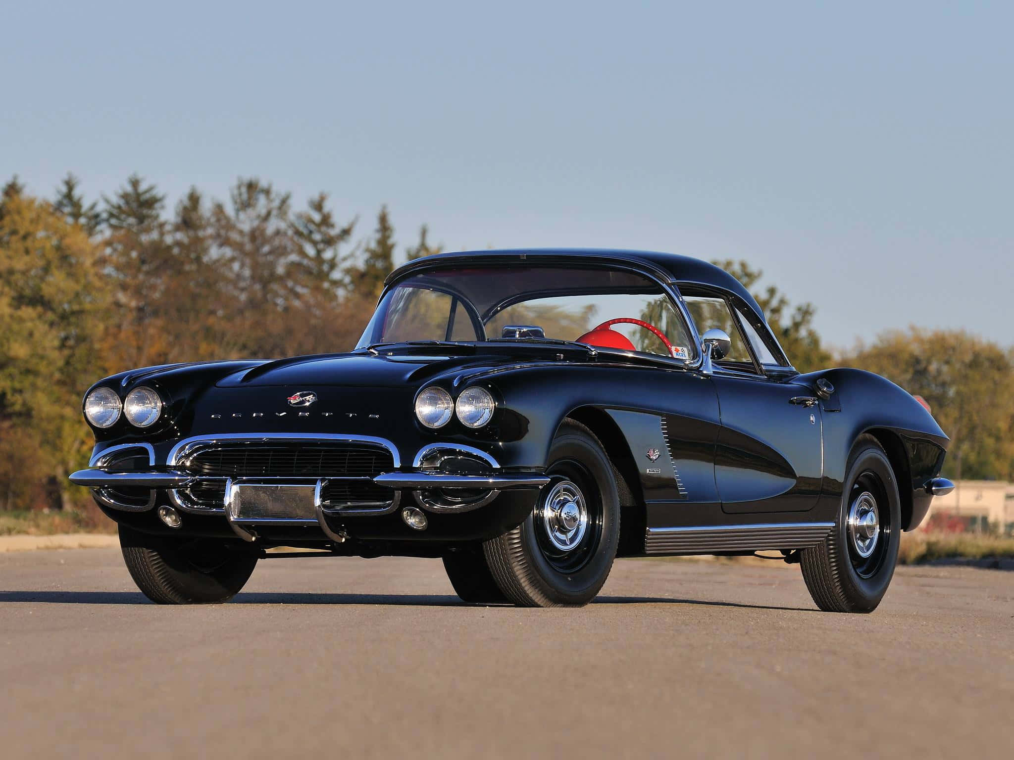 classic 桌布 壁紙 — 一架時尚的黑色經典Corvette跑車，帶有鍍鉻裝飾和紅色內飾，停在瀝青路上，背景是秋天的樹木。