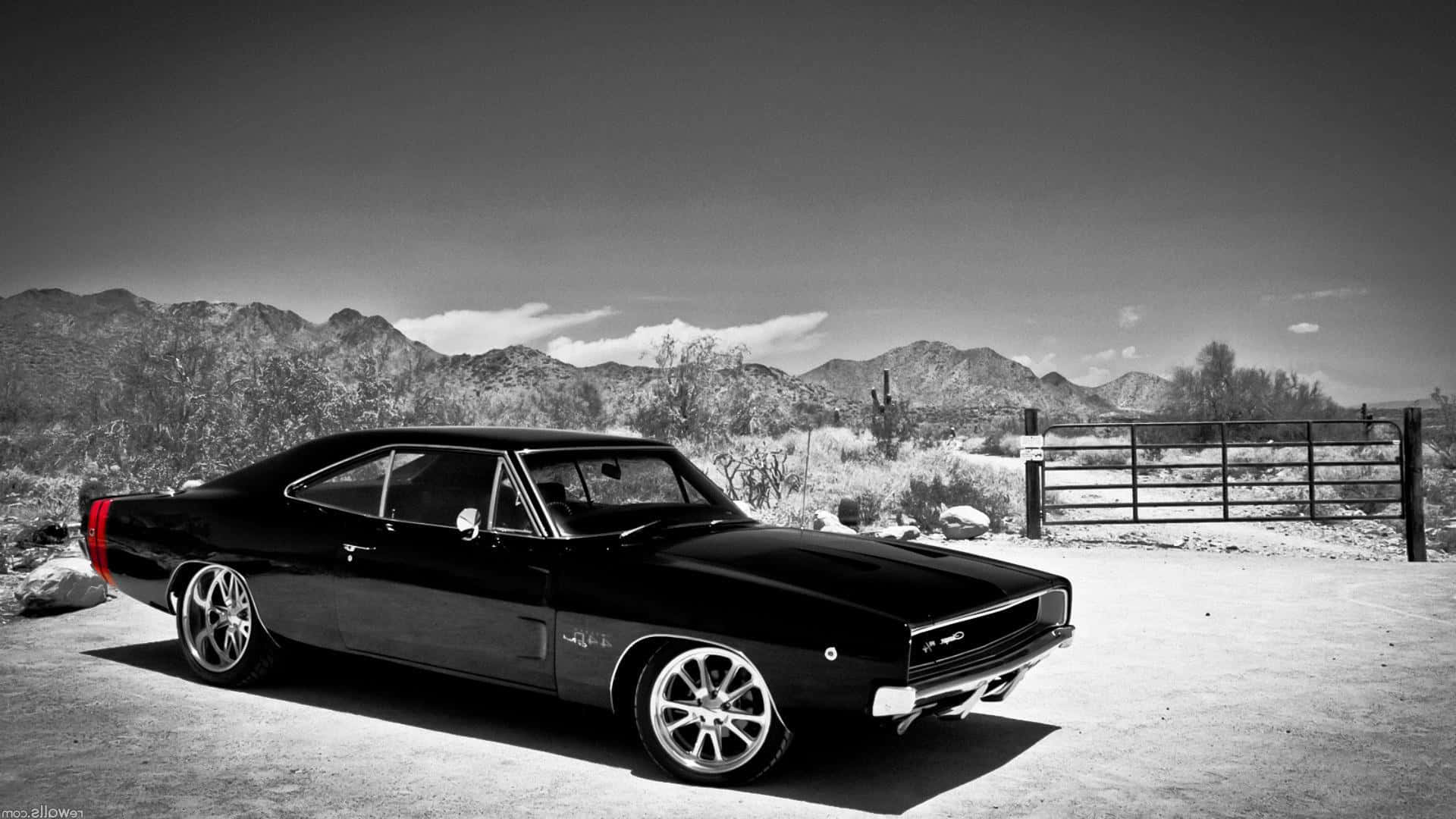 Dodge Charger 桌布 壁紙 — 一架時尚的黑色經典肌肉車停泊在沙漠景觀中，背景有山脈和大門，天空戲劇性十足。
