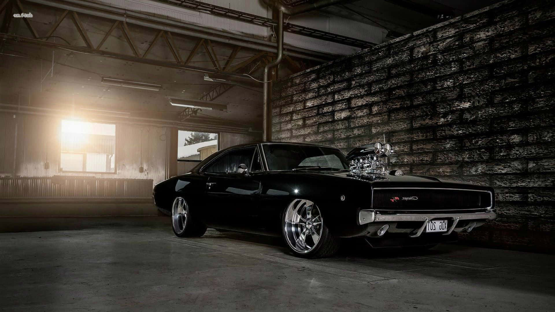 Dodge Charger 桌布 壁紙 — 一架時尚的黑色經典肌肉車配備鍍鉻增壓器，戲劇性地停在光線昏暗的工業車庫中，沐浴在溫暖的背光下。