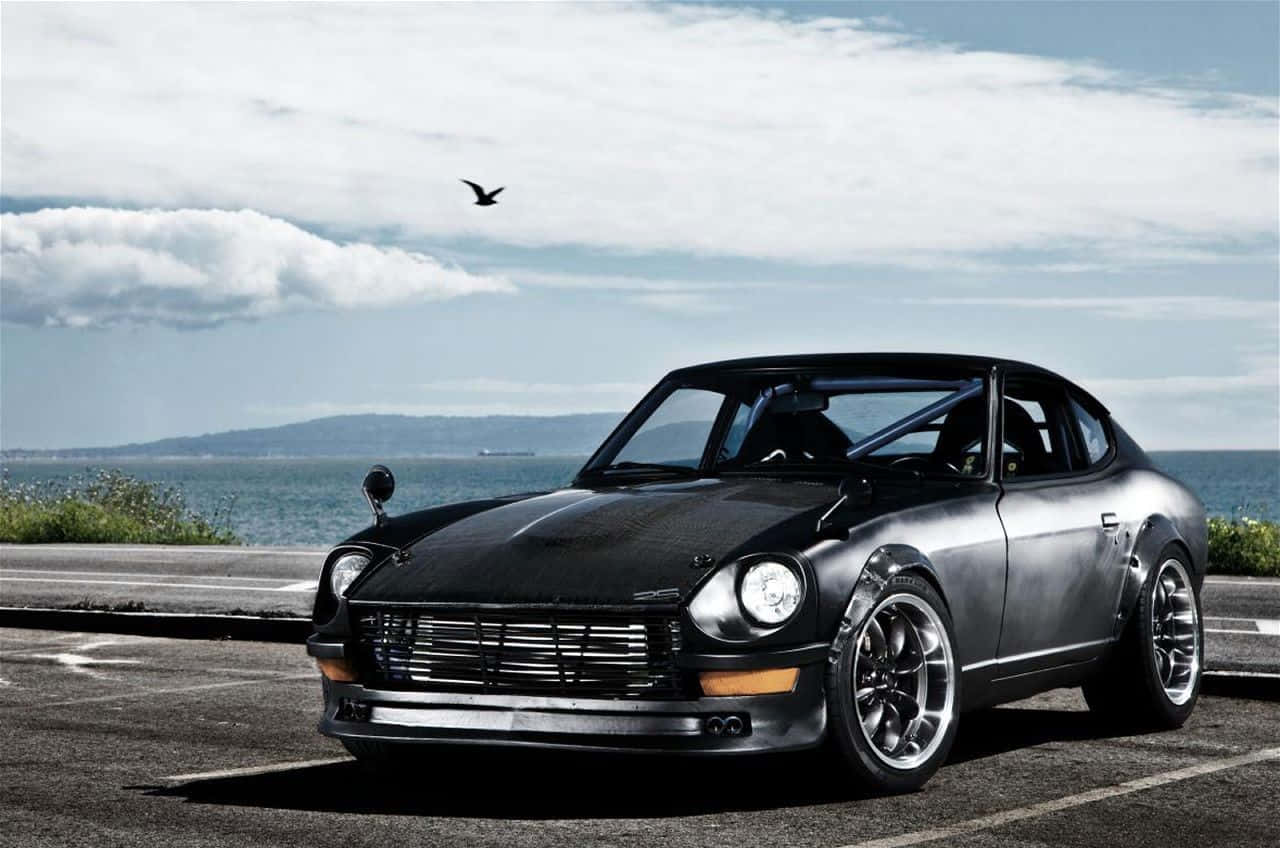 Datsun 桌布 壁紙 — 一架時尚的黑色經典跑車停泊在海岸公路上，背景是海洋和陰天。