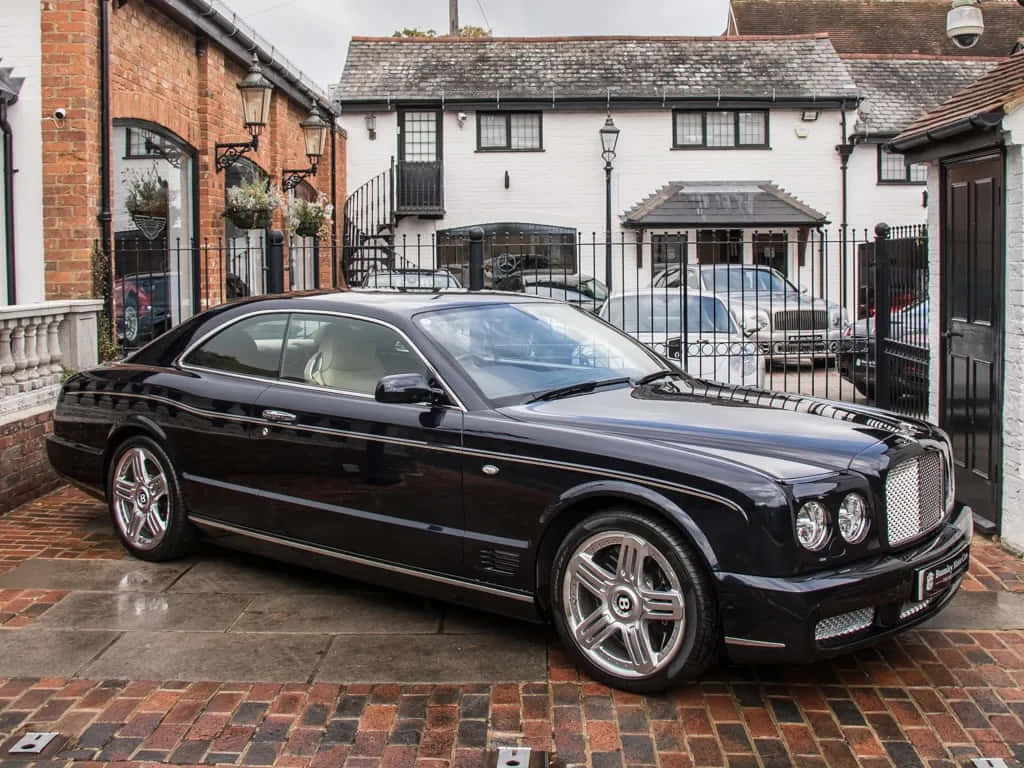 Bentley Brooklands 桌布 壁紙 — 一架時尚的黑色賓利 Continental GT 停泊在白色房屋前濕透的磚砌車道上，房屋帶有黑色欄杆。