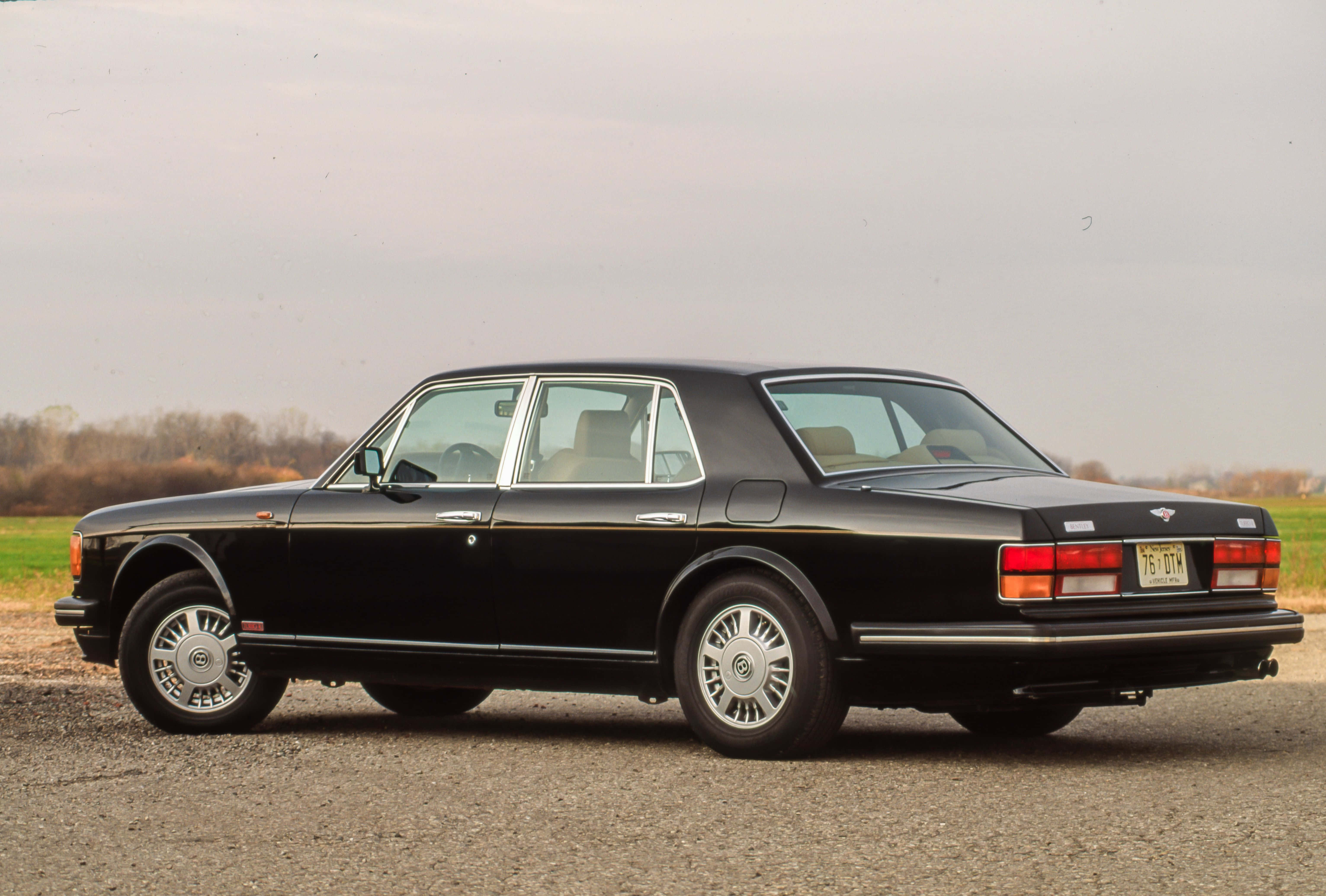 Bentley Turbo R 桌布 壁紙 — 一架時尚的黑色賓利房車停泊在碎石上，背景是柔和天空和光禿禿的樹木。