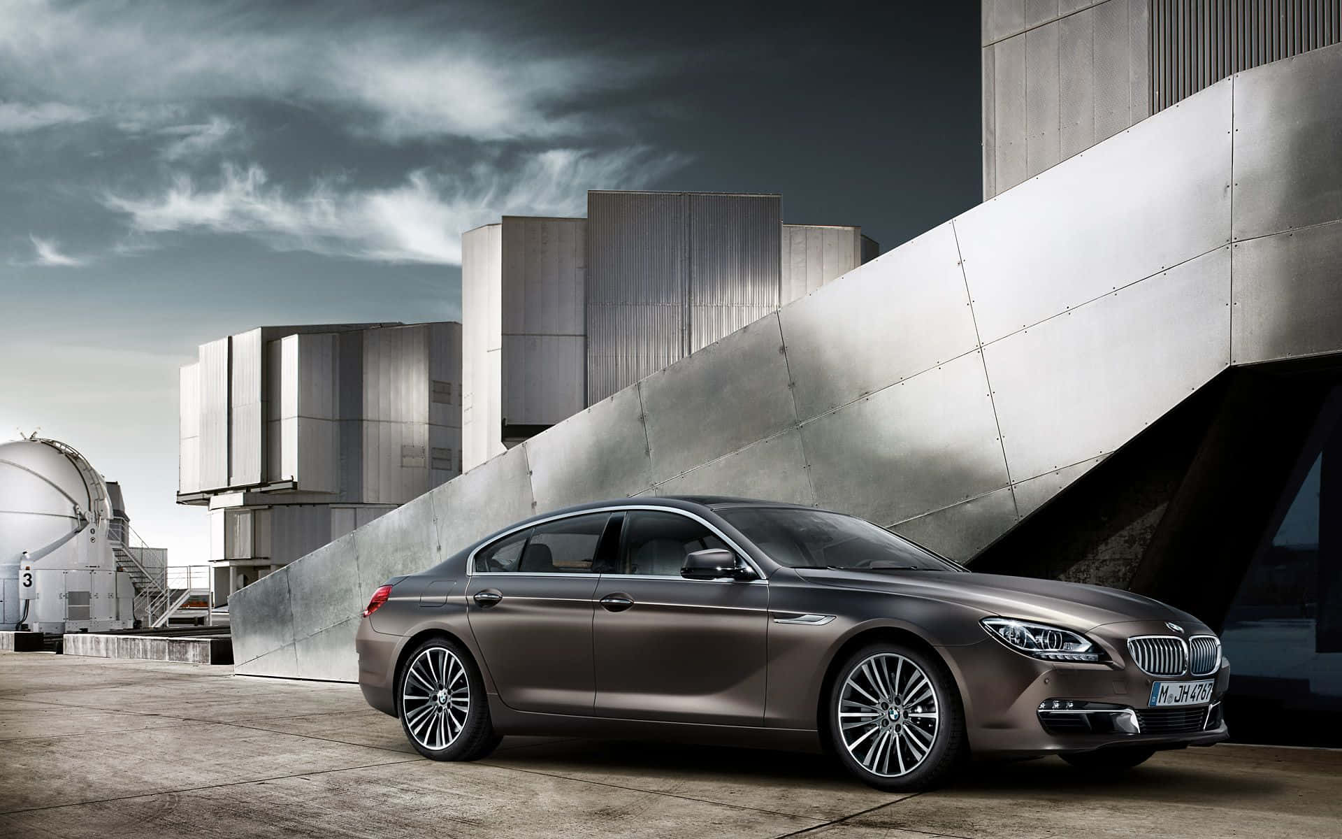 Bmw 6 Series 桌布 壁紙 — 一架時尚金屬棕色BMW 6系轎車停泊在現代棱角建築旁，天空多雲。